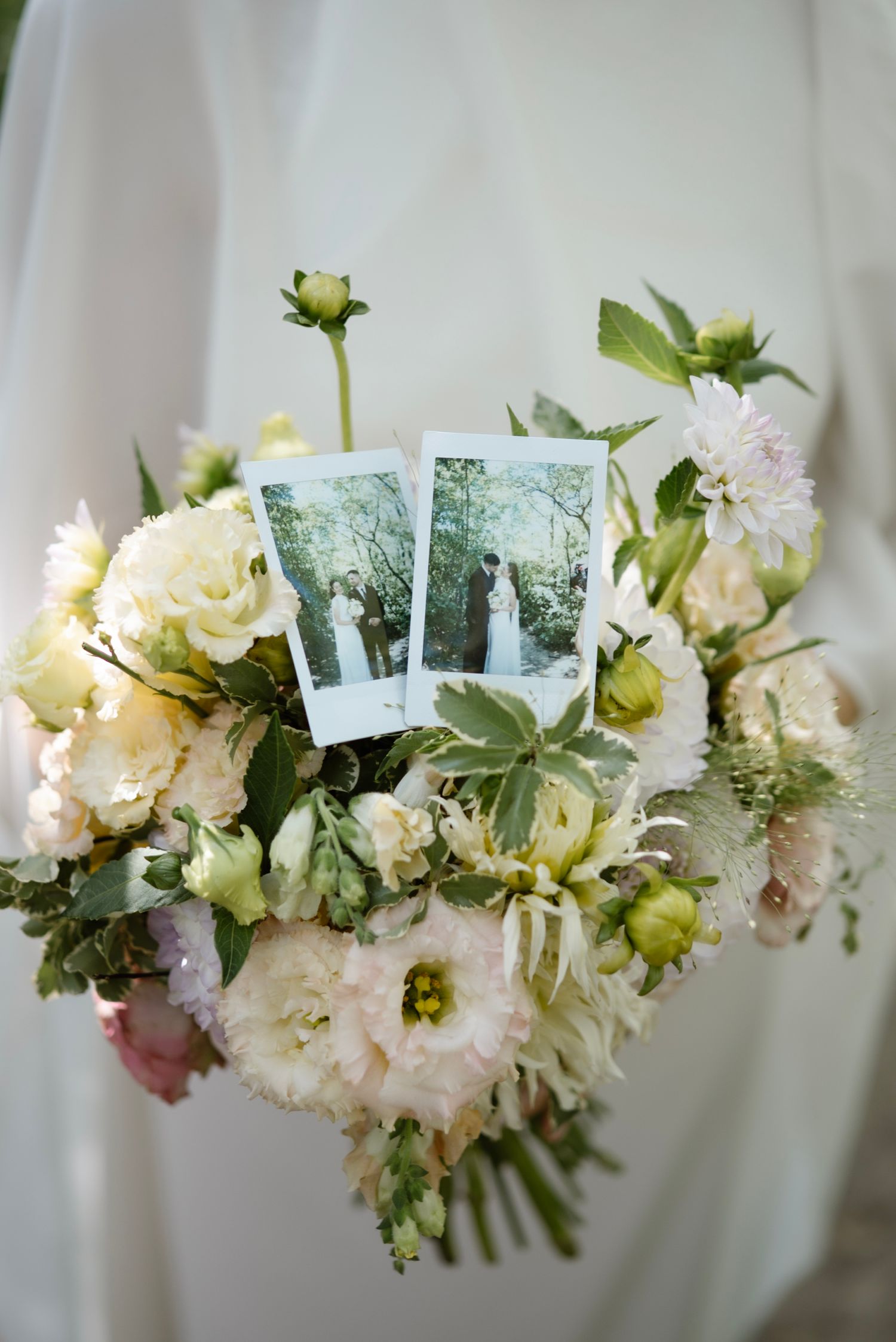 Romantic wedding bouquet with white and pink flowers featuring two Polaroid photos of a bride and groom tucked among the blooms.