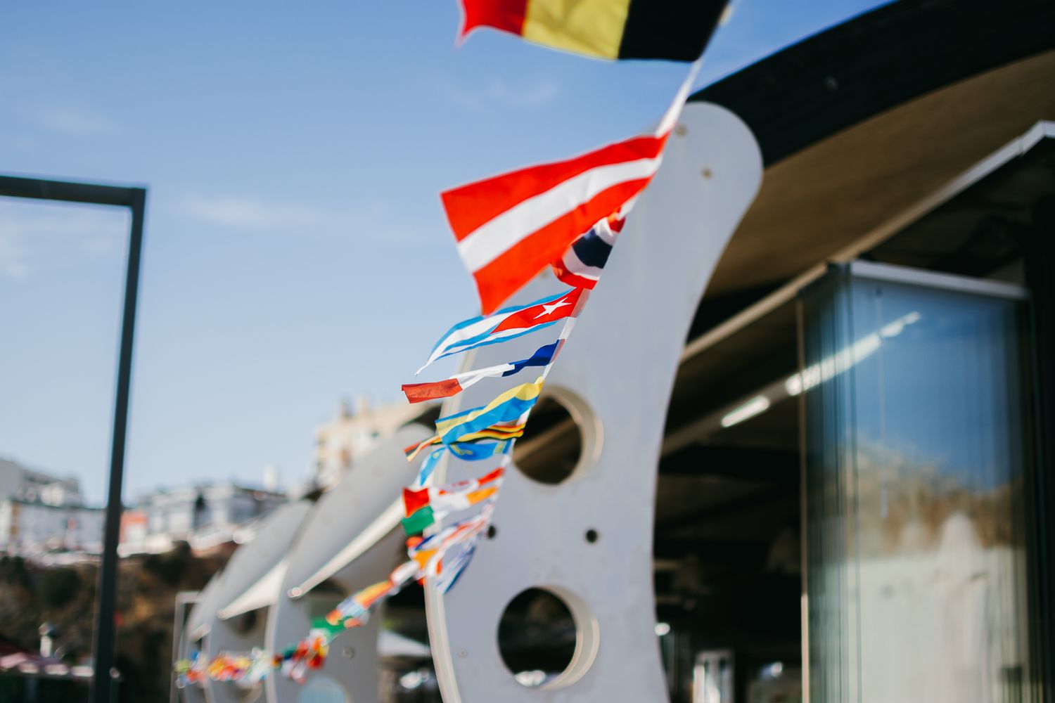 Colorful international flags waving against a bright blue sky.