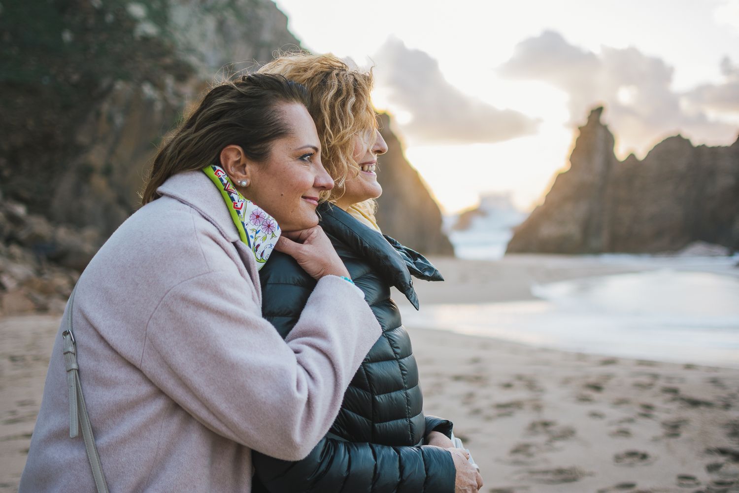 Couple embracing on a beach during golden hour sunset with ocean waves and cliffs in the background.