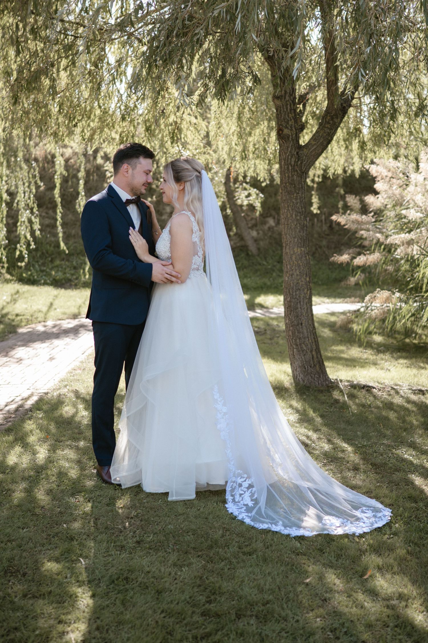 A romantic wedding photoshoot under willow trees in a serene outdoor setting.