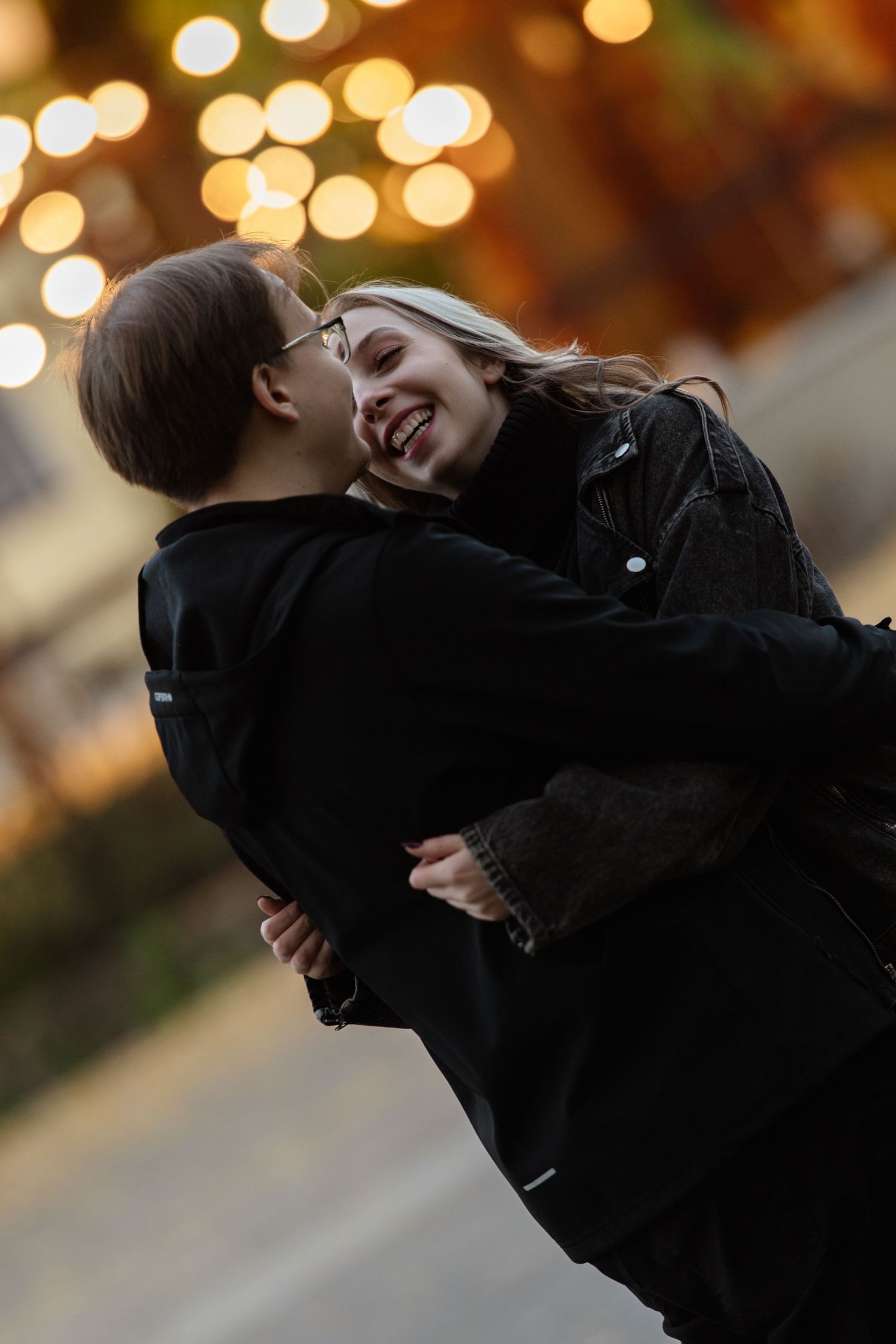 Couple embraces joyfully against a warm bokeh background during golden hour.