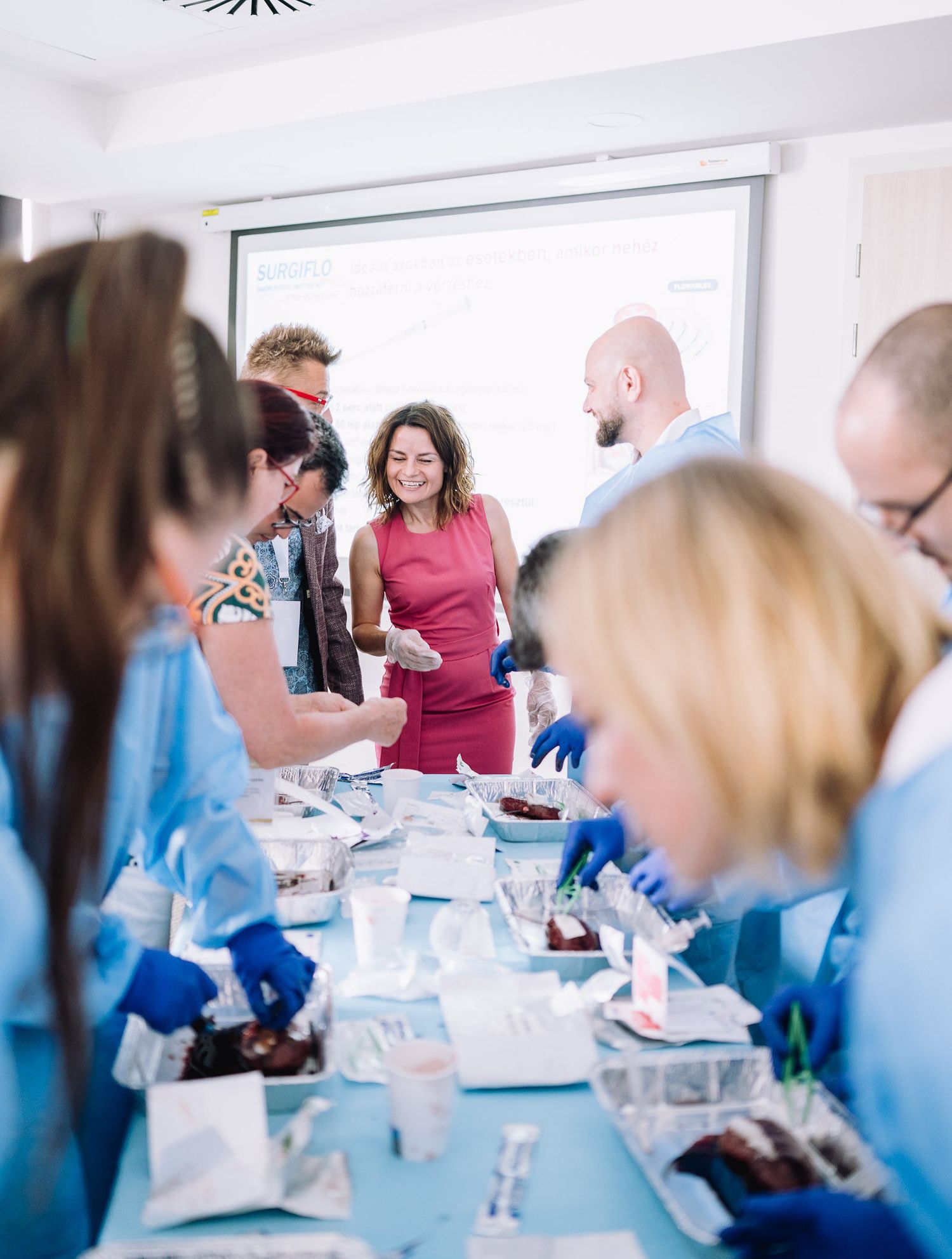 Business meeting attendees gathered around tables in a bright conference room.