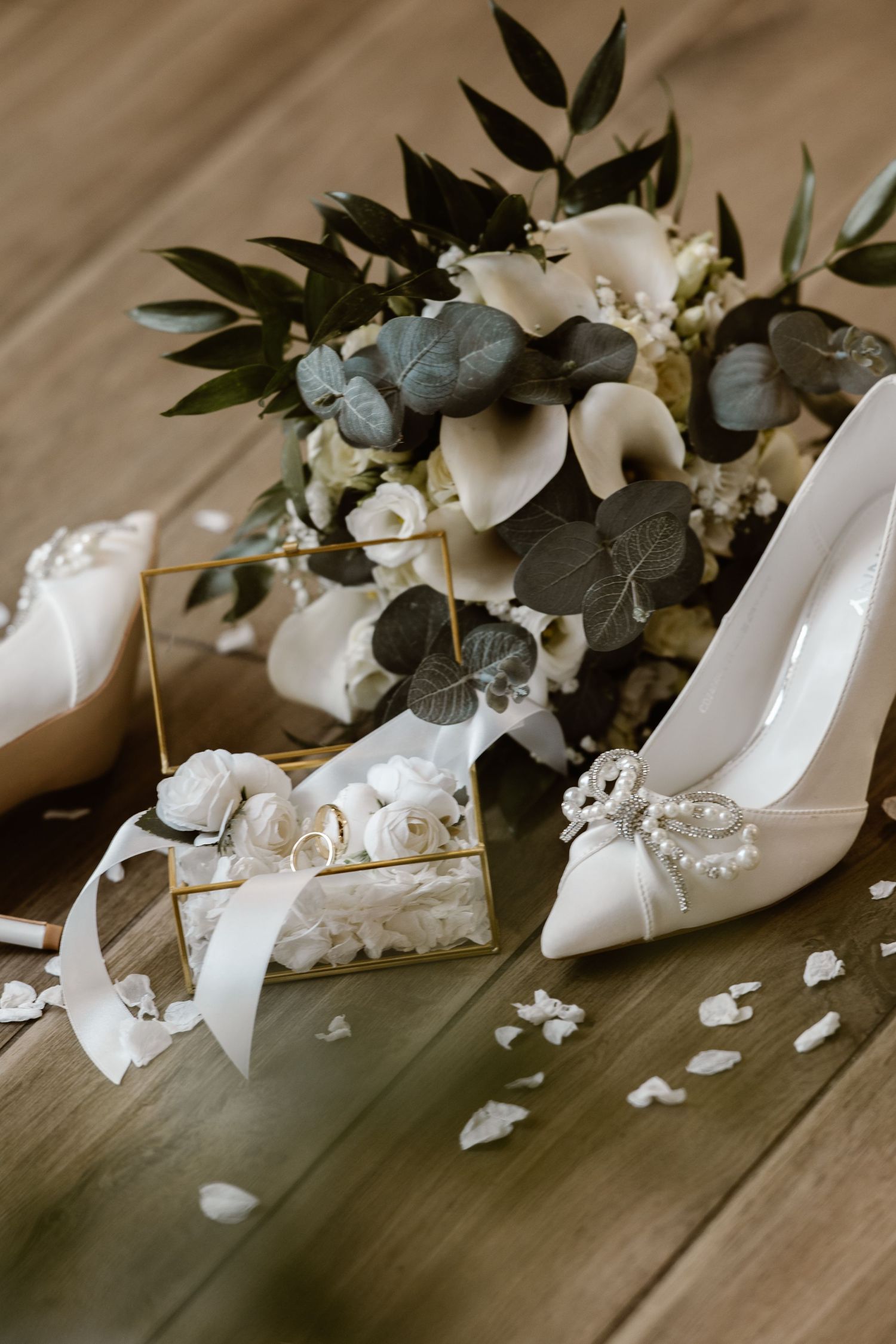 White bridal shoes with delicate floral decorations and pearls arranged on a wooden floor.