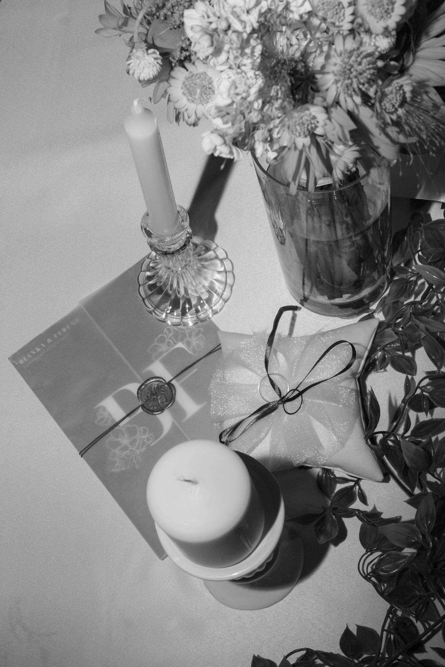 Black and white still life of wedding details including flowers and paper goods on white surface.