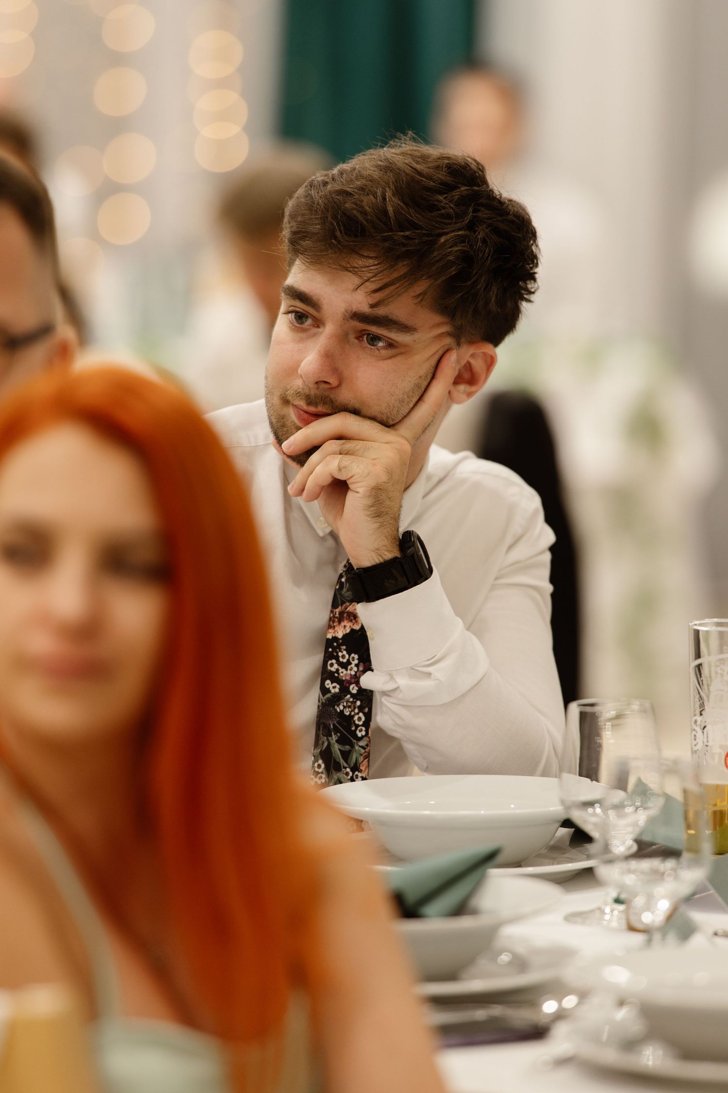 Guests seated at elegant dinner table with bokeh lights in background.