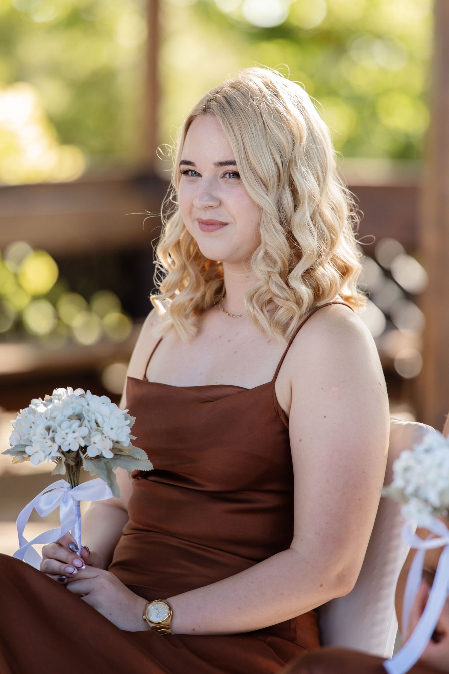 Person in brown dress holding white flowers during outdoor wedding ceremony.