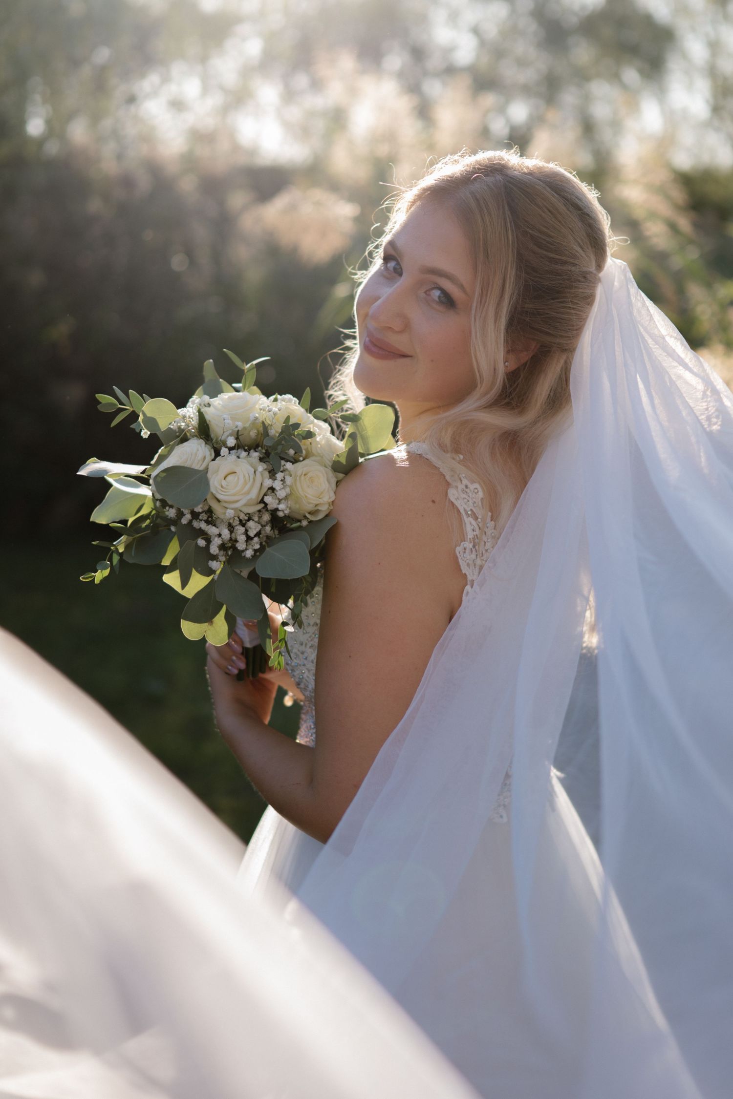 A bridal bouquet of white roses and eucalyptus against a flowing white wedding dress.