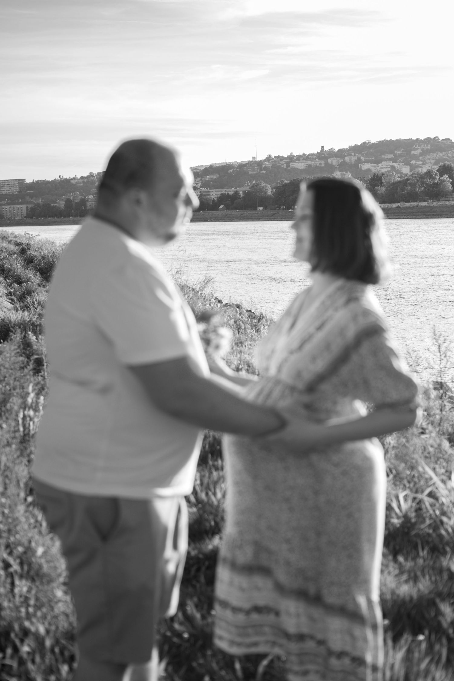 A soft focus black and white photo of a couple by a lake during sunset.