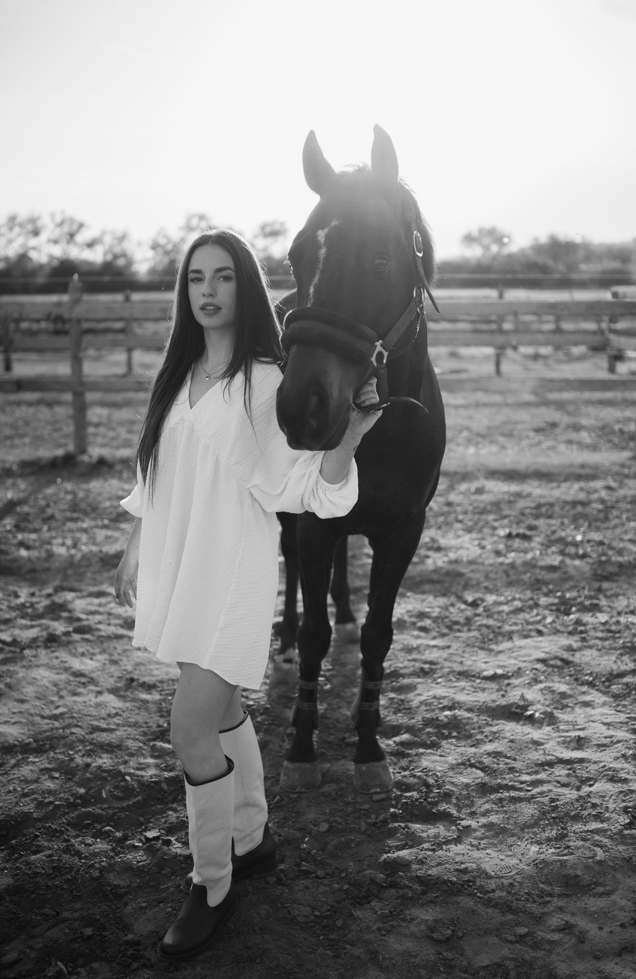 Black and white portrait of person with horse in rustic farm setting.