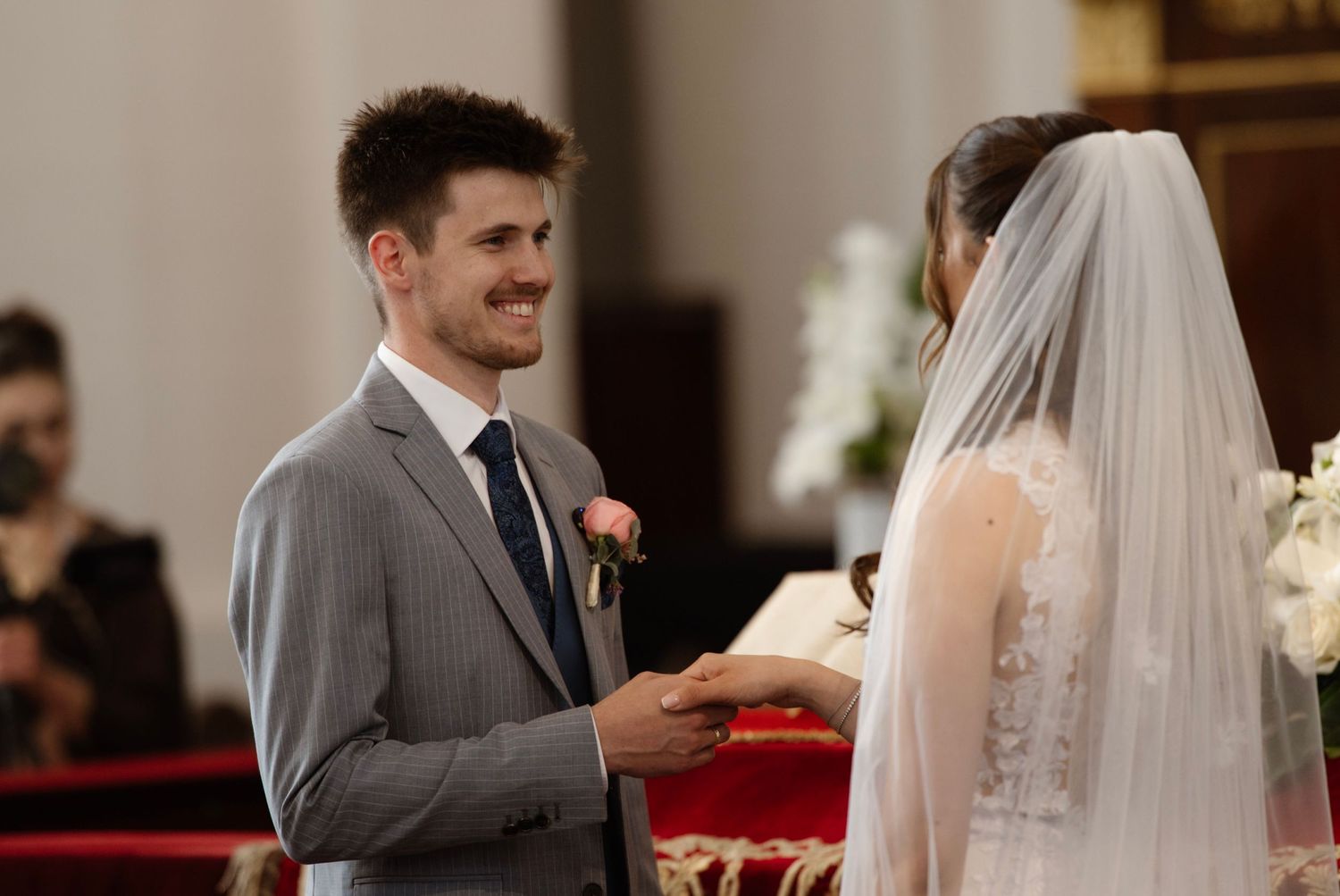 Groom smiling at bride during wedding ceremony in church, exchanging rings at the altar.
