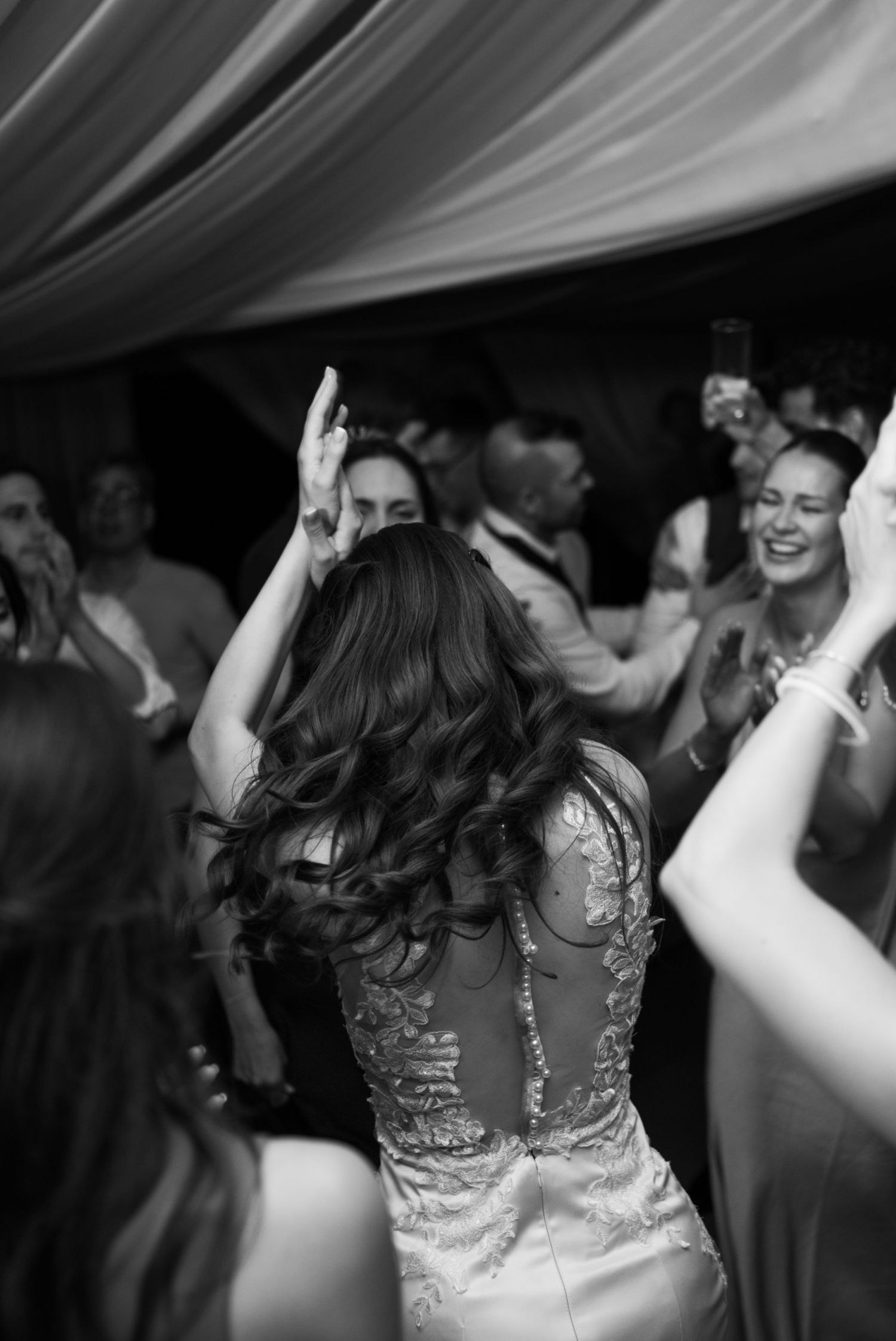 Black and white photo of bride dancing with guests at lively wedding reception celebration.