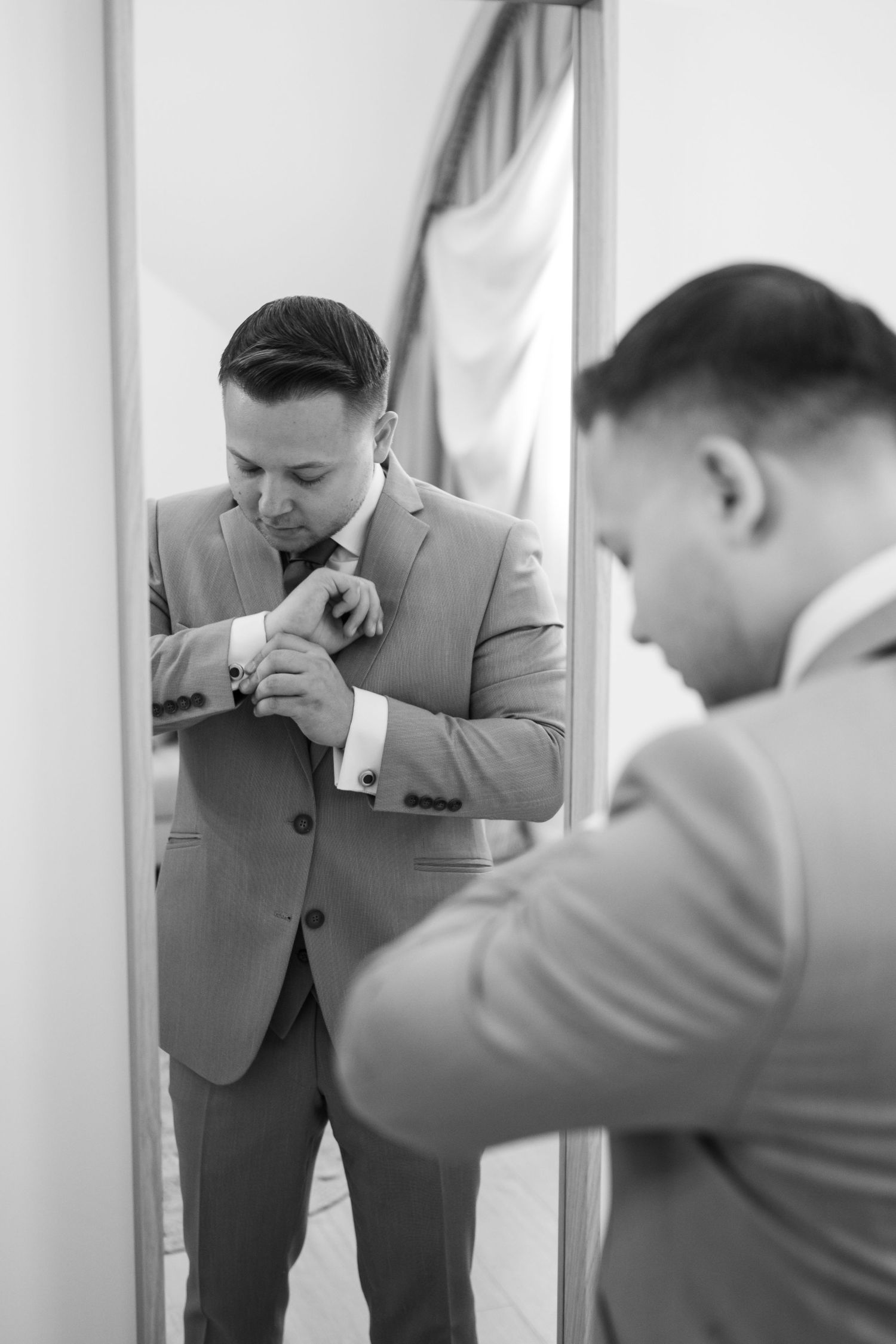 Person in grey suit checking appearance in mirror during wedding preparation.