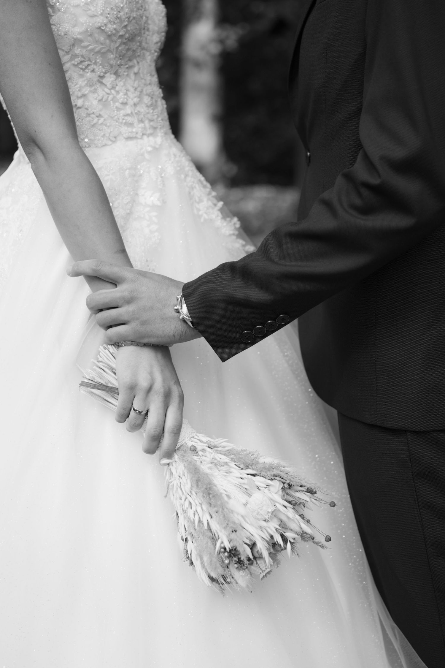 Close-up black and white detail of hands against a white wedding dress with lace details.