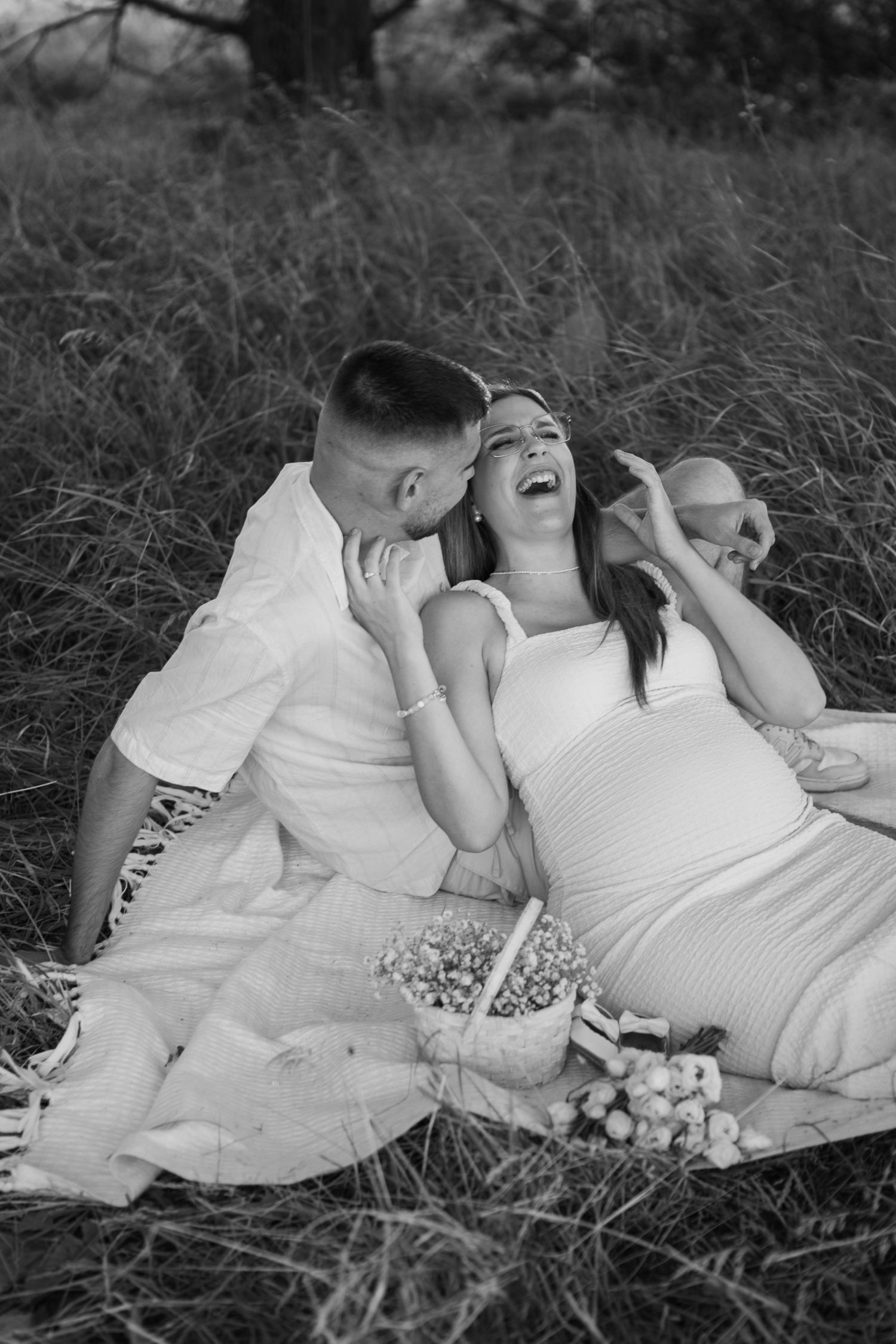 Couple lying together on a blanket in tall grass sharing intimate black and white moments.
