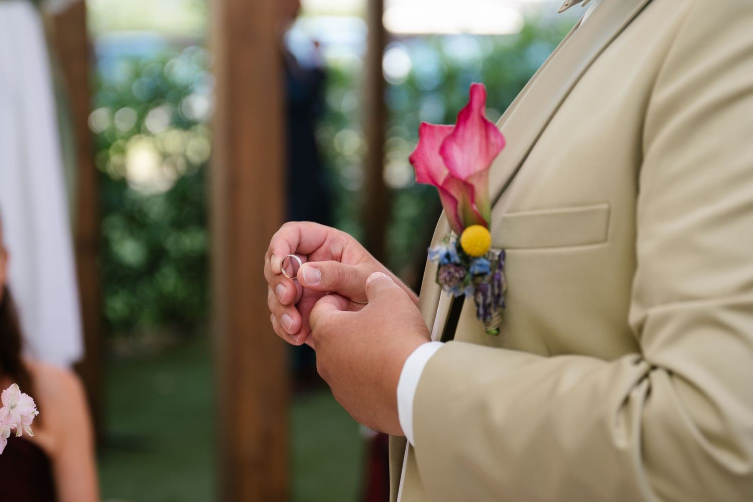 Close-up shot of a pink boutonniere being pinned to a tan suit jacket.