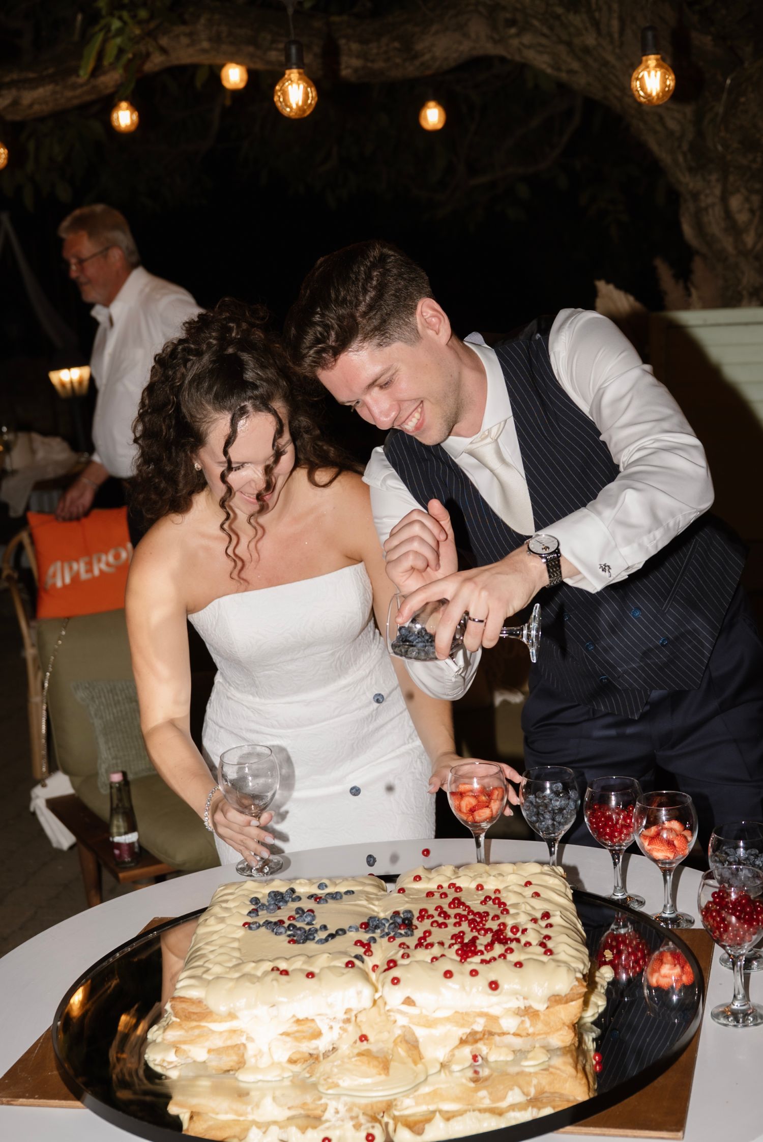 Bride and groom cutting a decorated wedding cake together at an outdoor evening reception.