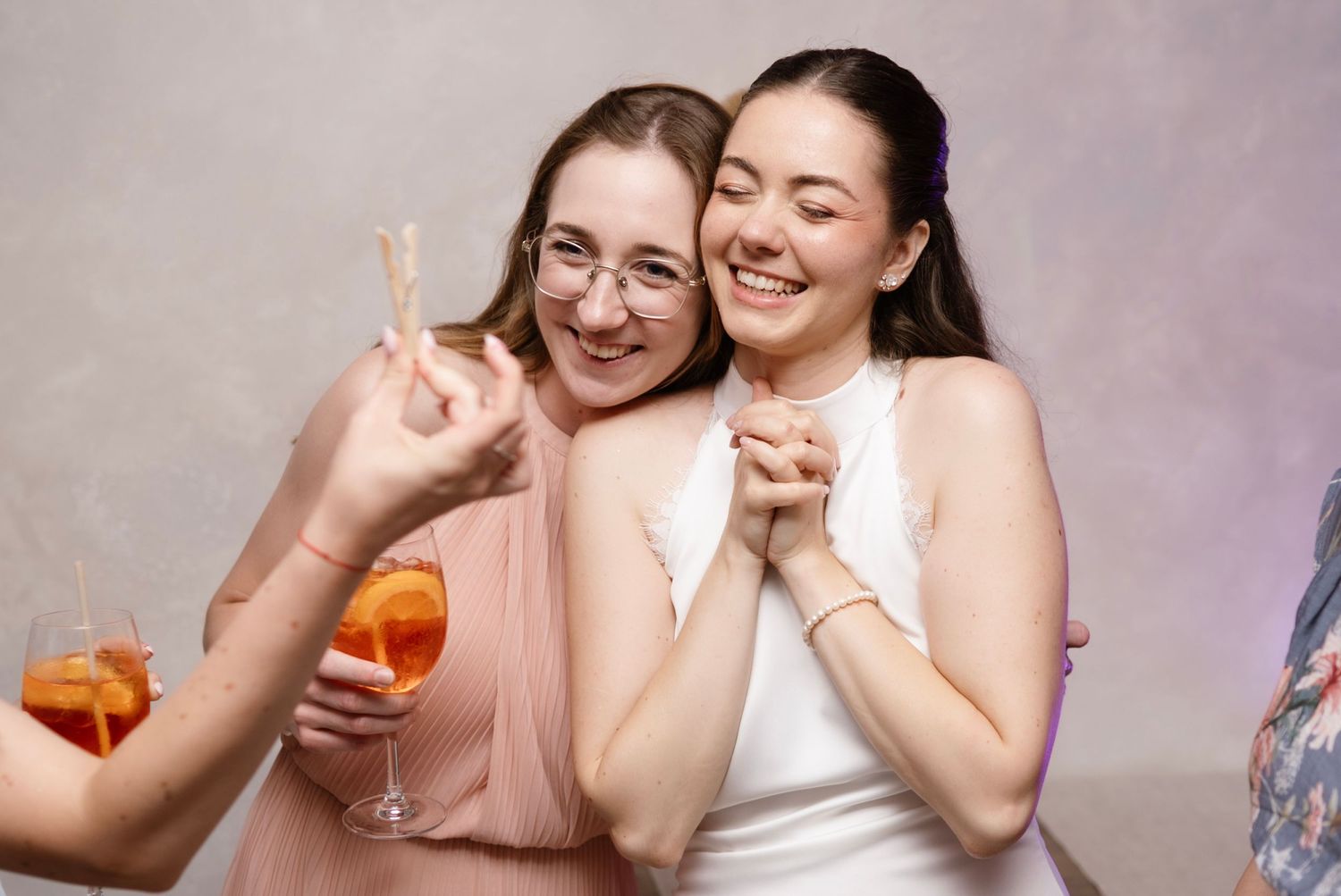 Two smiling women posing together at a party, one holding an Aperol Spritz cocktail in a wine glass.