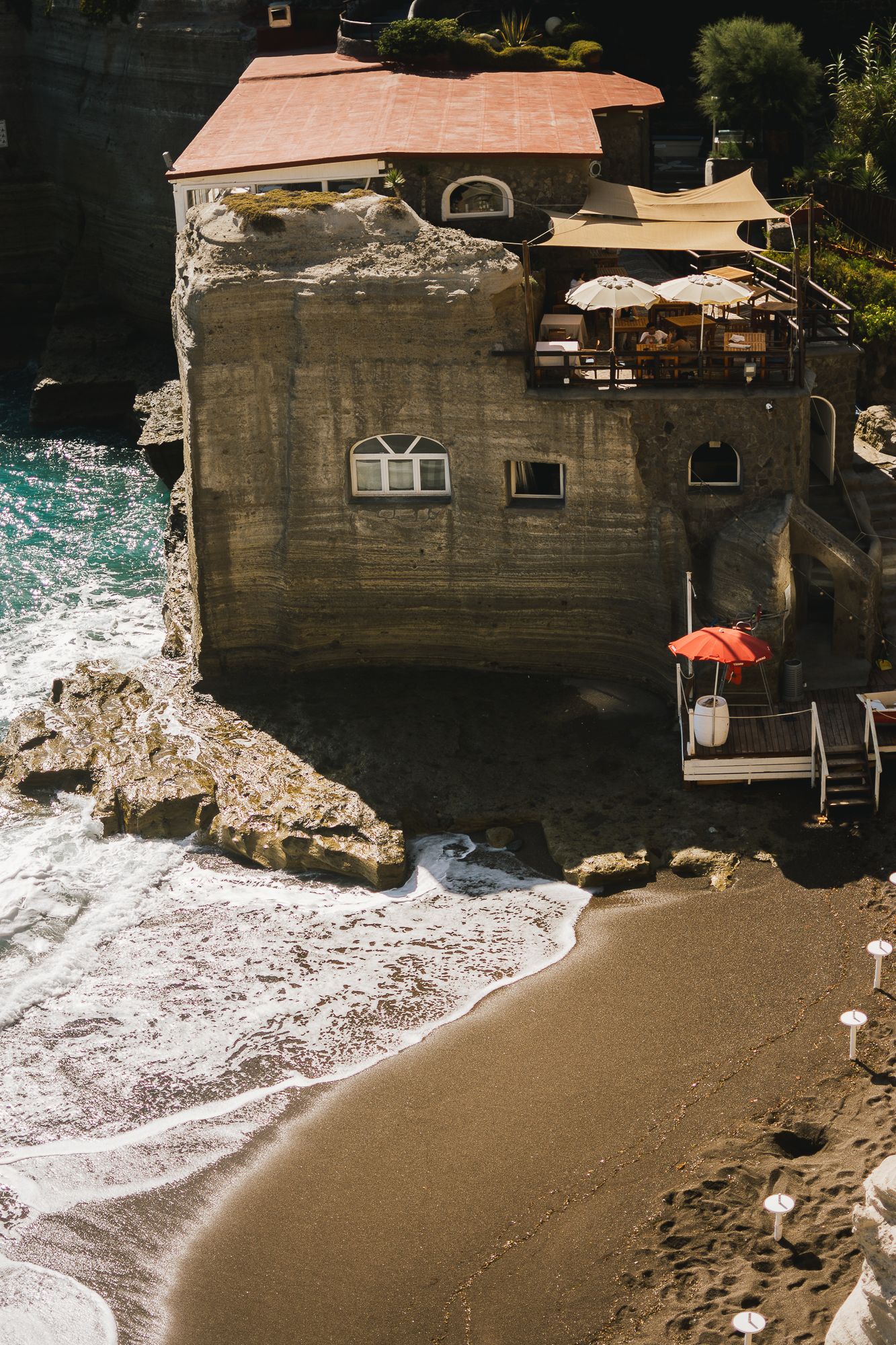 Coastal house built on rocky cliffs with waves crashing against the shore below.