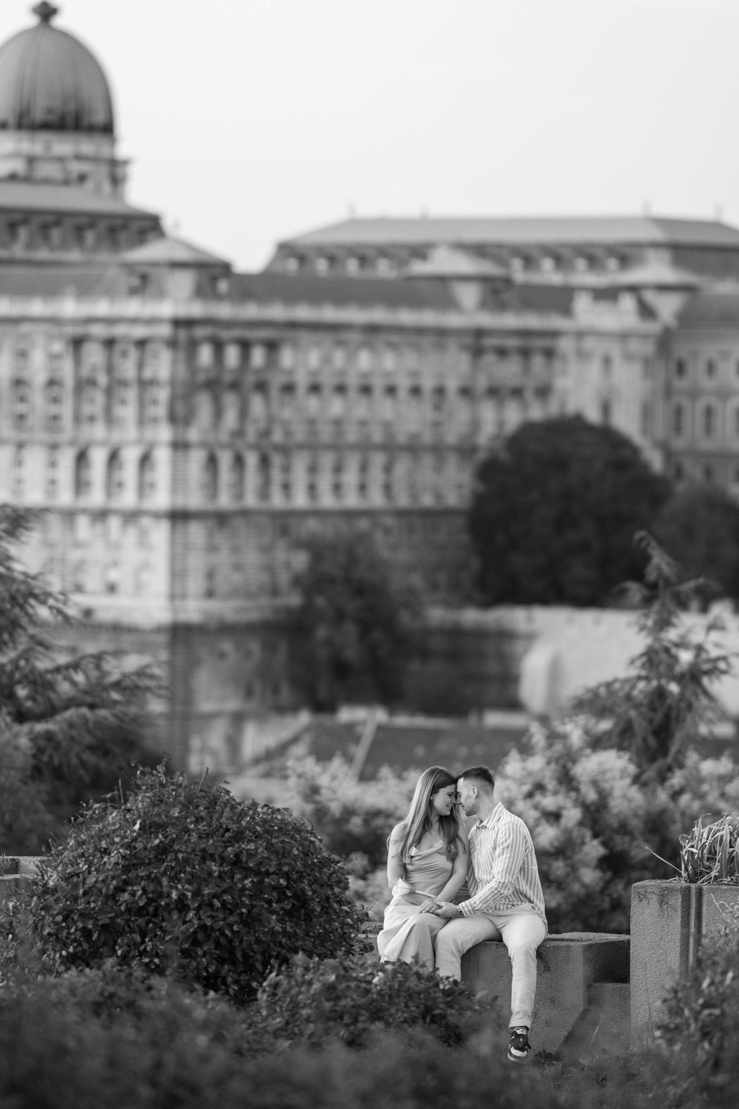 Romantic couple sitting together with historic European architecture in background.