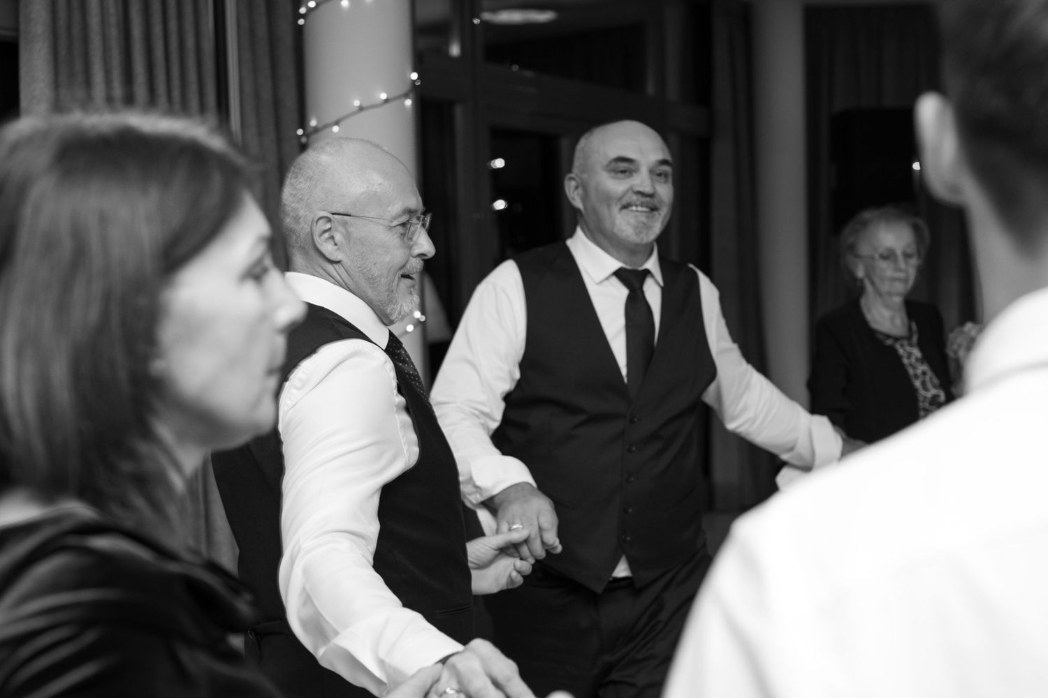 Black and white photo of guests dancing and celebrating at a wedding reception.