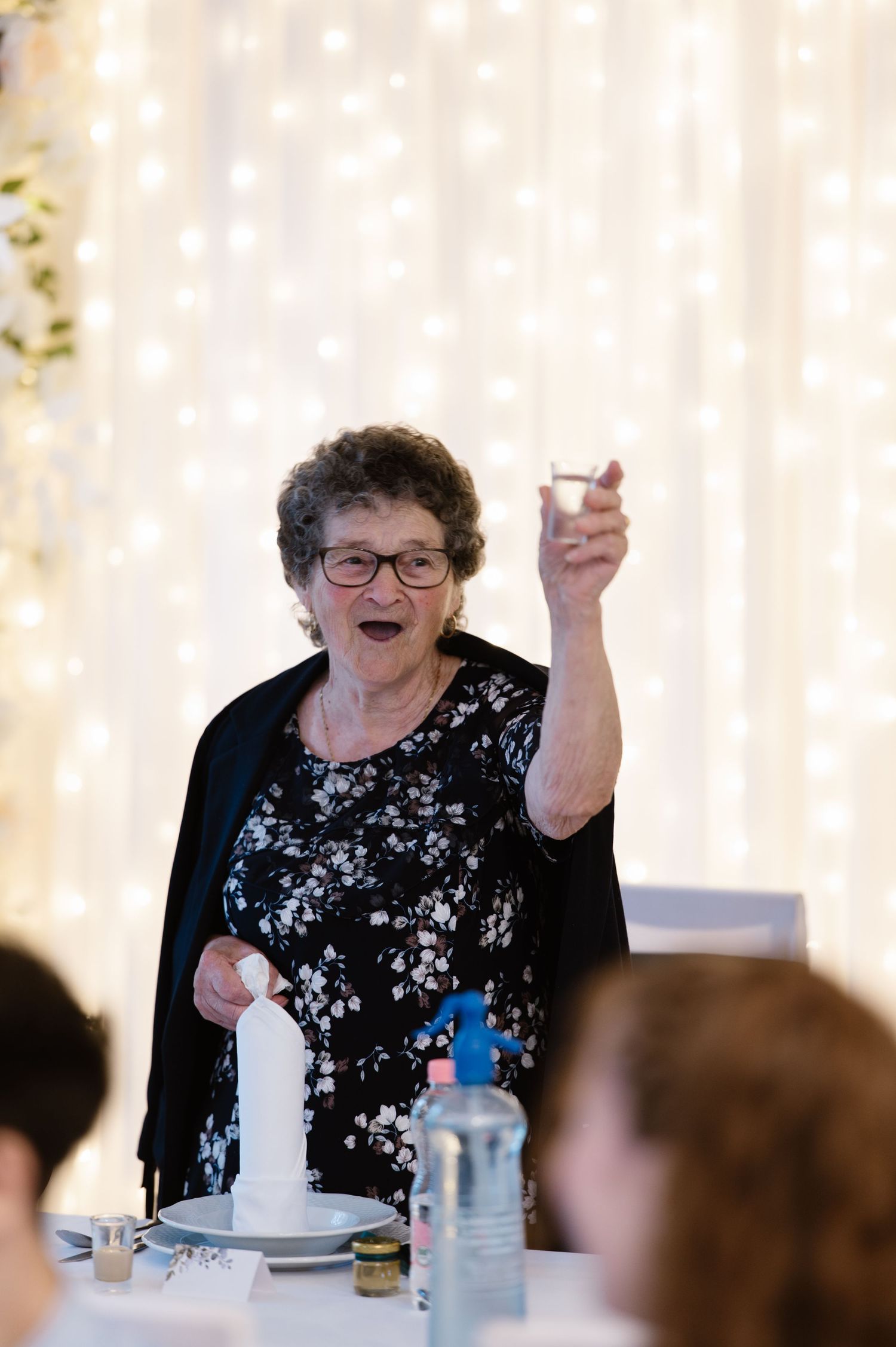 Wedding guest celebrates joyfully at reception with sparkly backdrop.