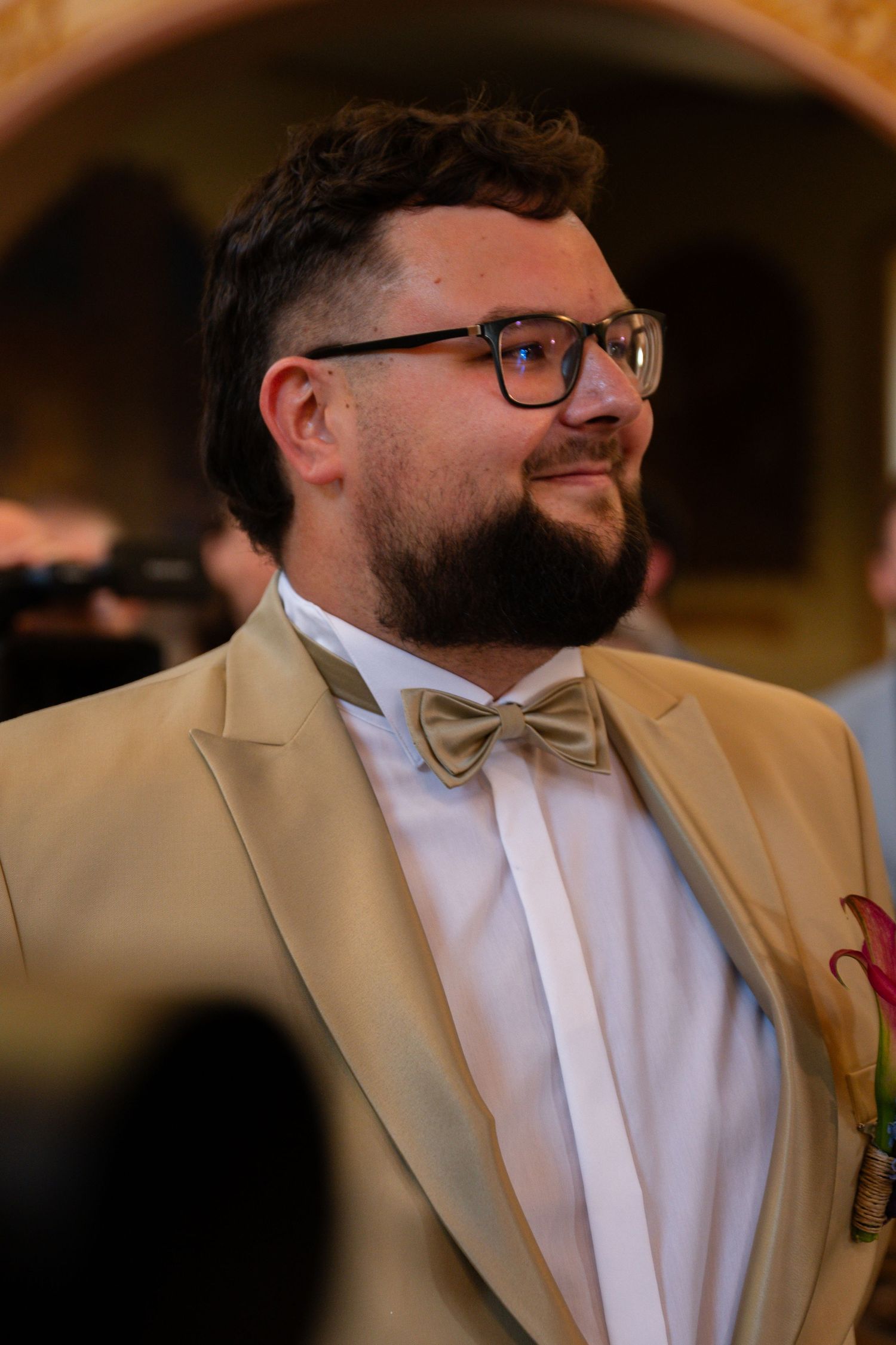 Side profile of someone wearing a tan suit jacket and bowtie at a formal event.