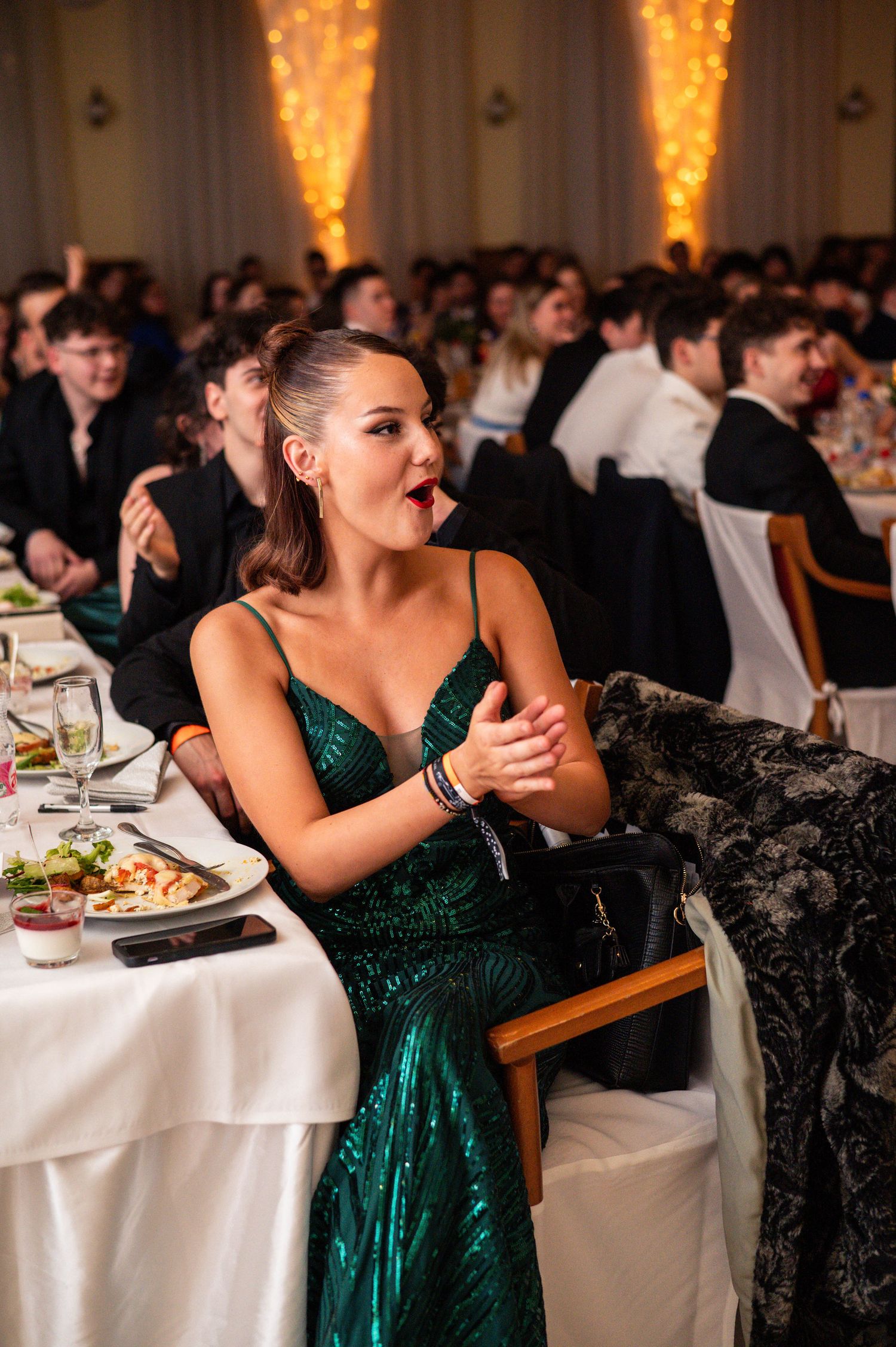 Guest in emerald green dress seated at elegant wedding reception table with white linens.