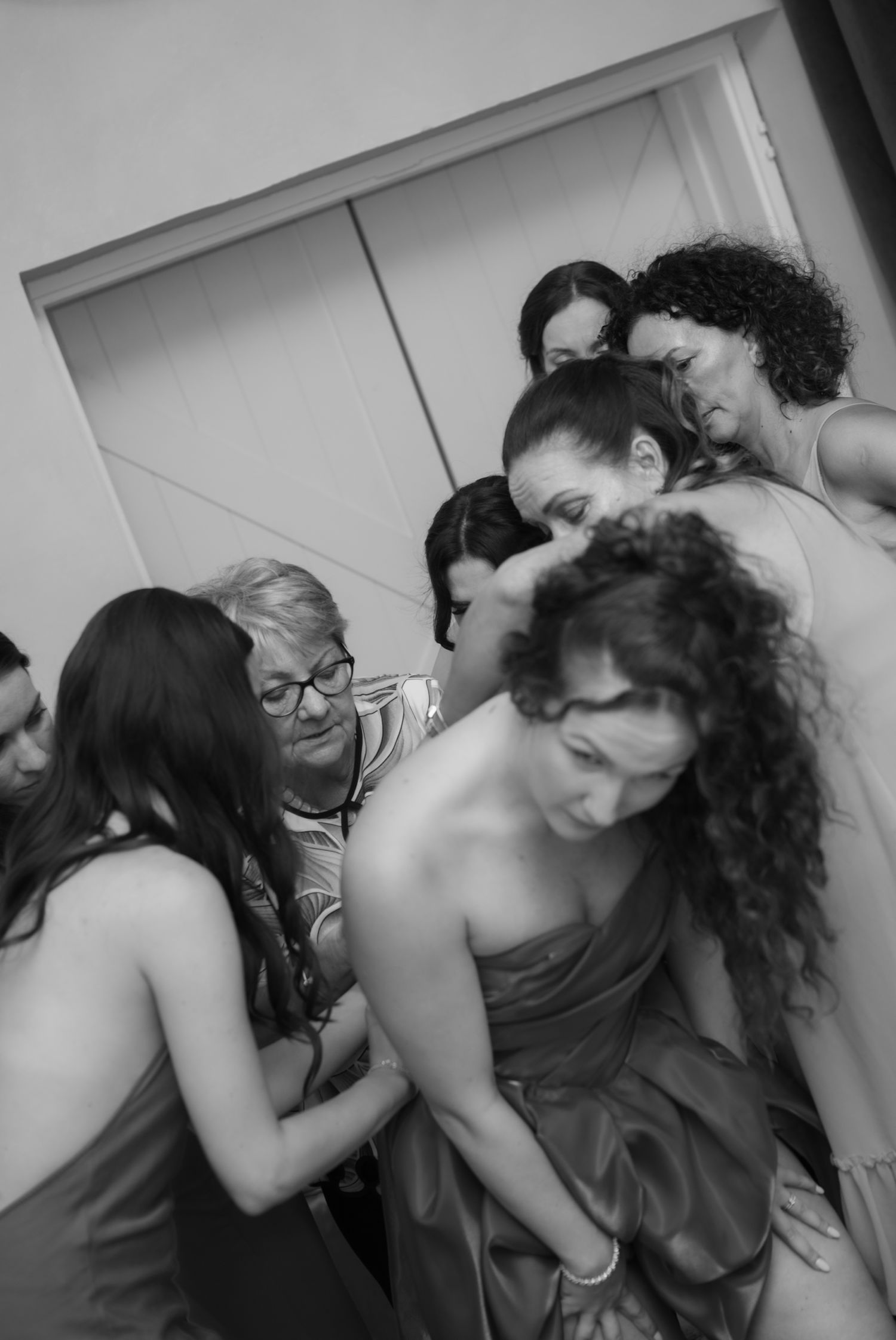 Black and white photo of women helping a bridesmaid get dressed before a wedding.