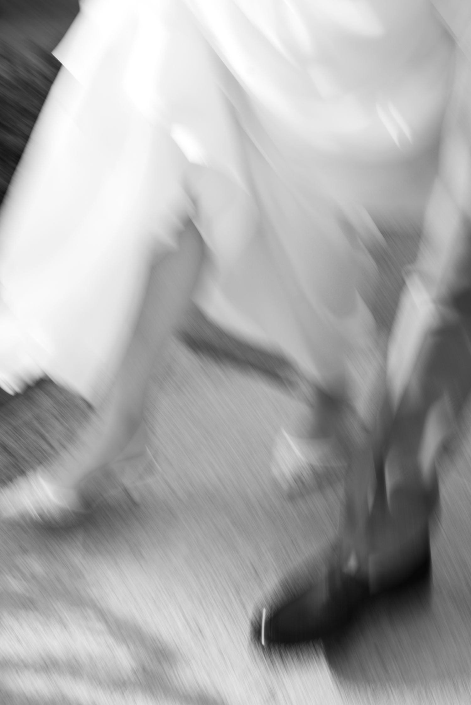 Blurred black and white photo of a bride in a white wedding dress and heels walking, captured with motion blur effect.