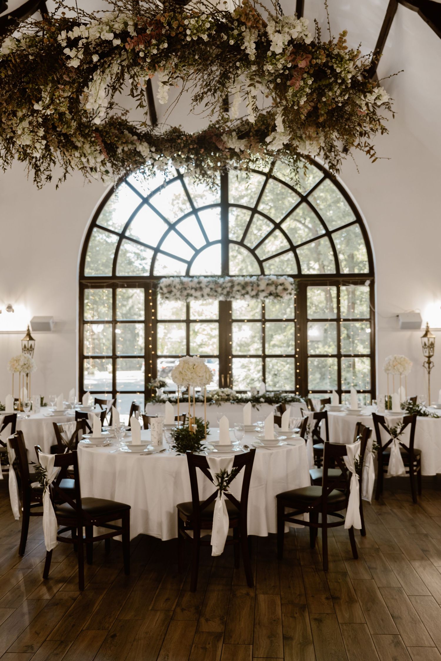 Elegant wedding reception venue with arched windows and rustic dried floral ceiling decorations.