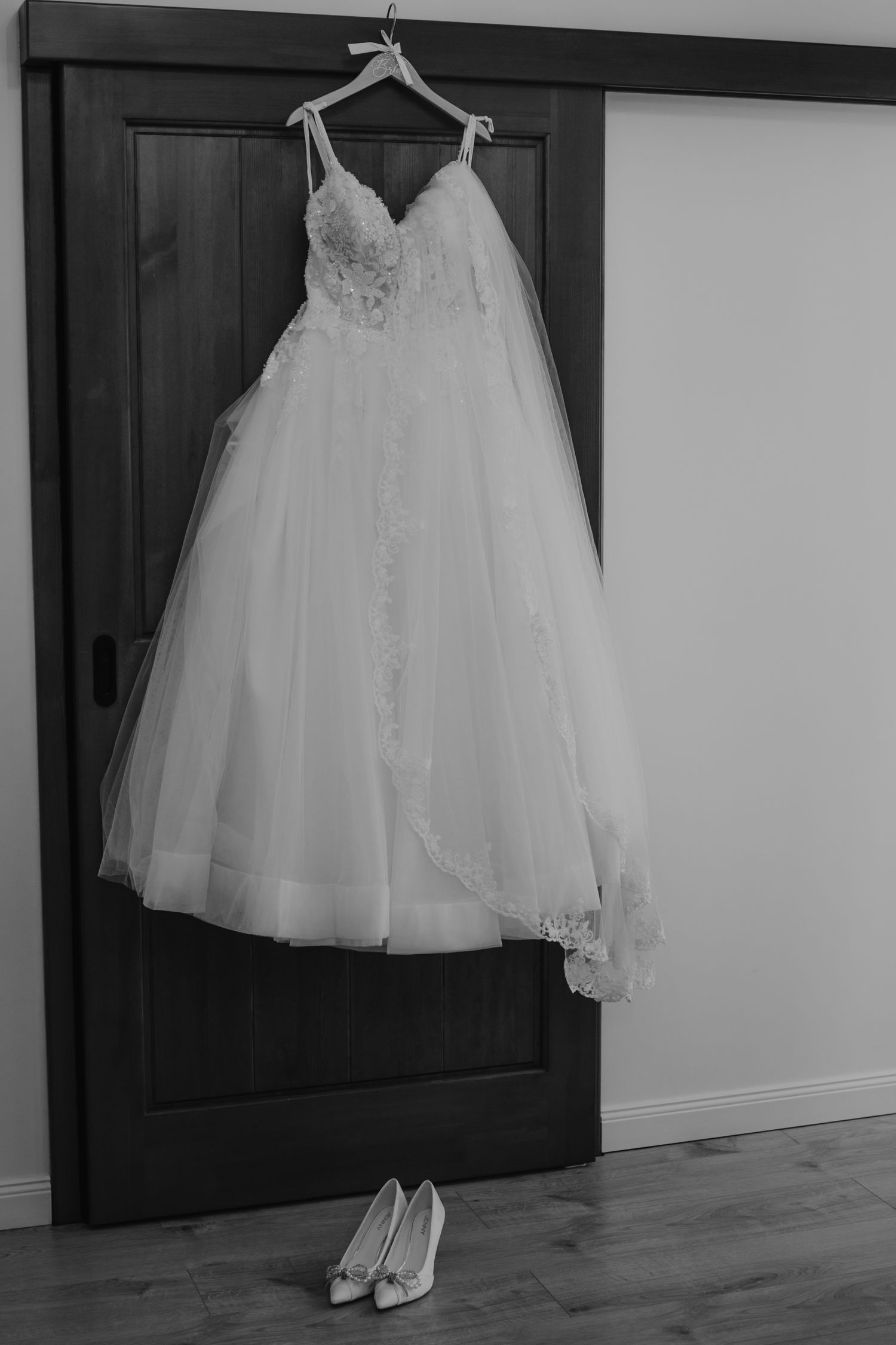 Elegant white wedding dress and shoes displayed on hanger against dark wooden door.