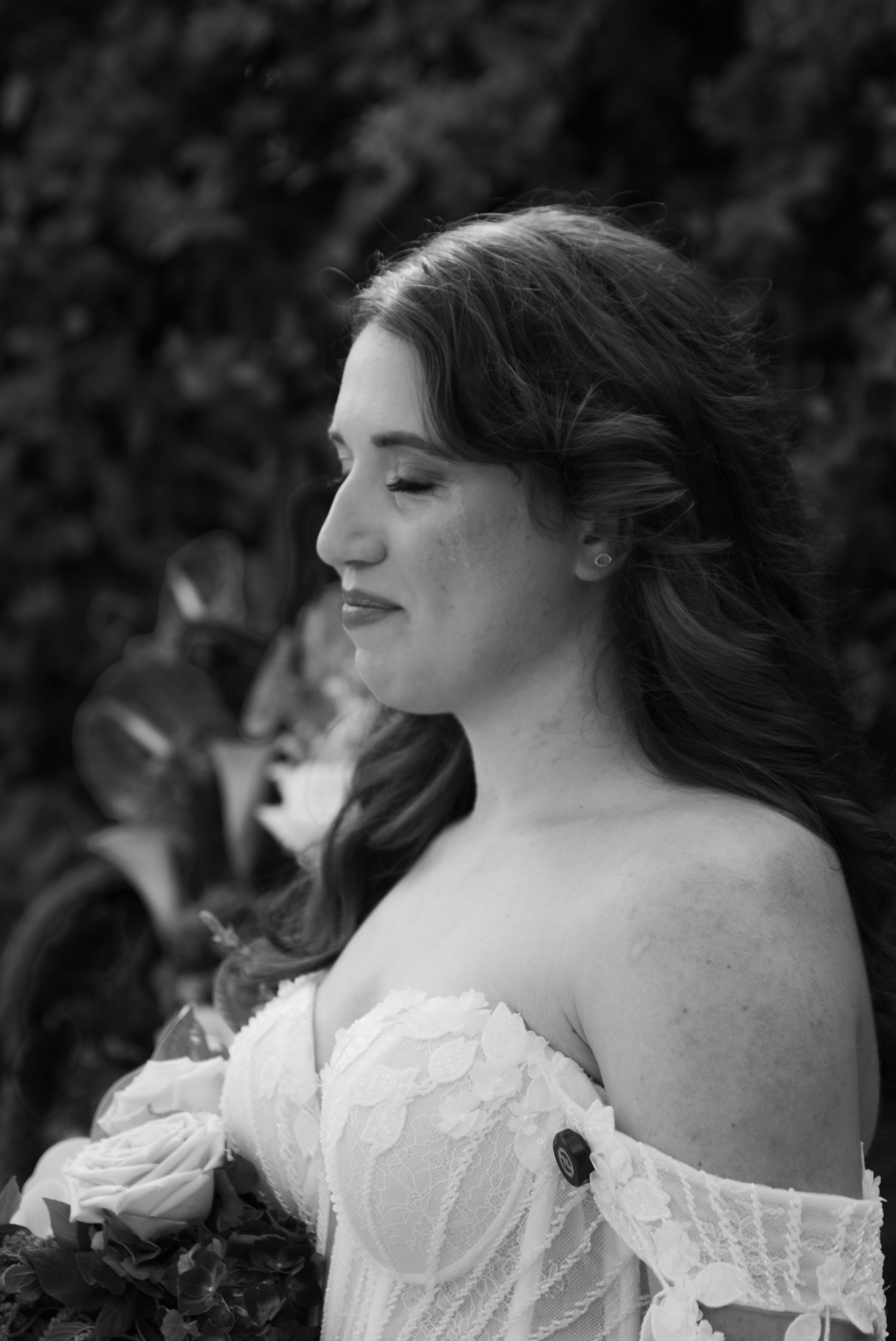 Black and white portrait of a bride with long hair in an off-shoulder wedding dress holding a bouquet.
