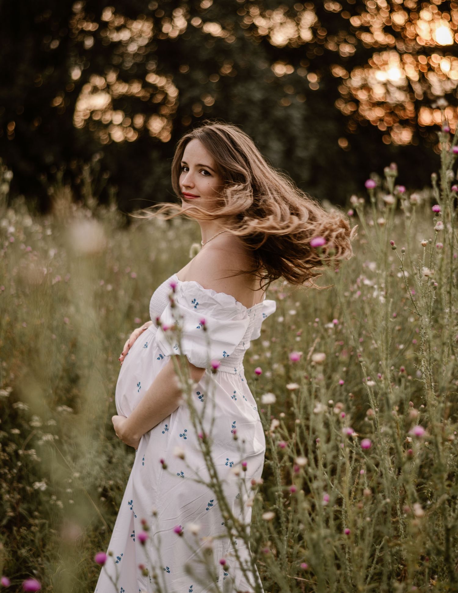 Woman in floral dress spins gracefully in meadow at golden hour.