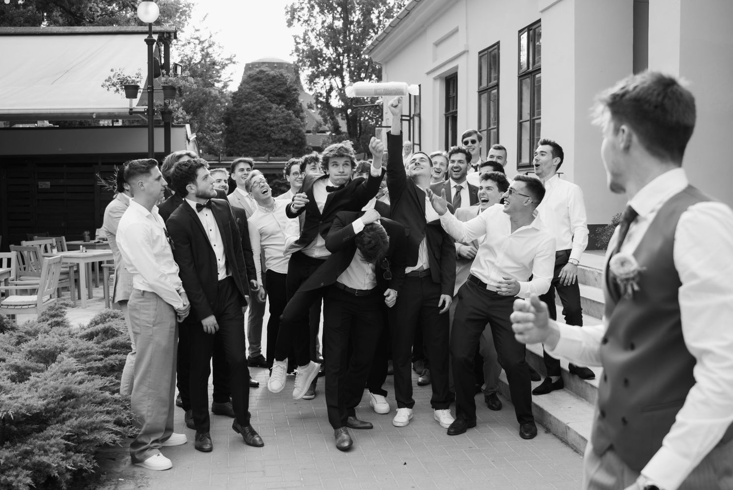 Black and white photo of groomsmen celebrating at a wedding reception, with one man triumphantly raising an object.