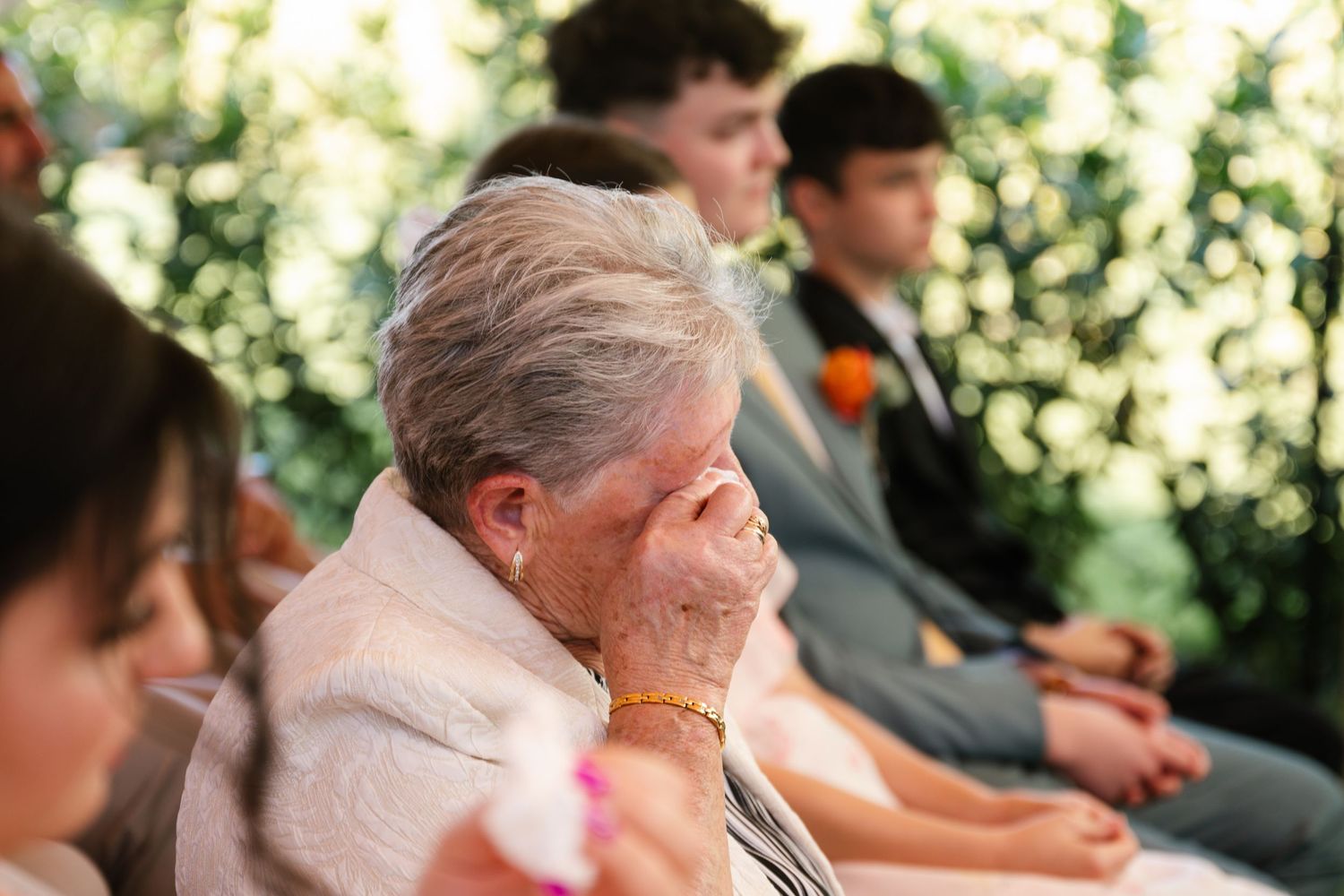 Wedding guests seated outdoors in a garden ceremony with natural greenery in the background.