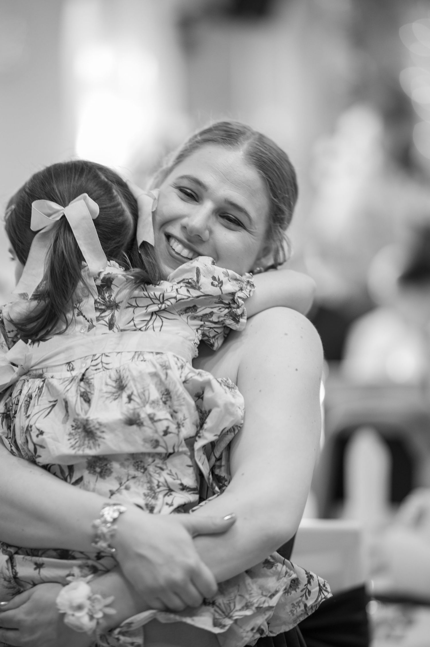 Young girls in floral dresses hug during a special celebration.