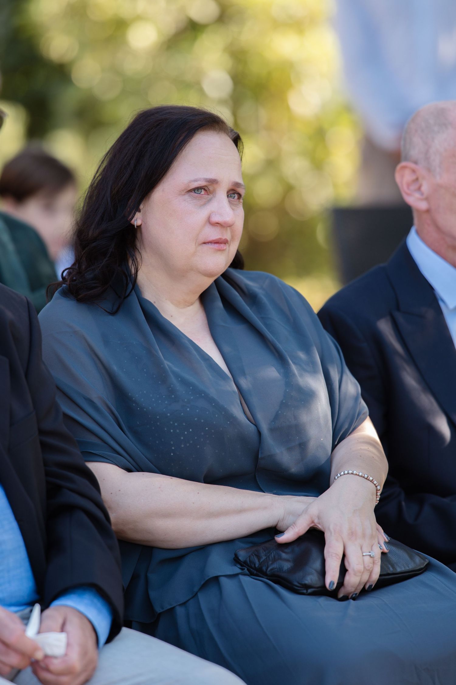 Wedding guests in formal attire seated outdoors during a ceremony.