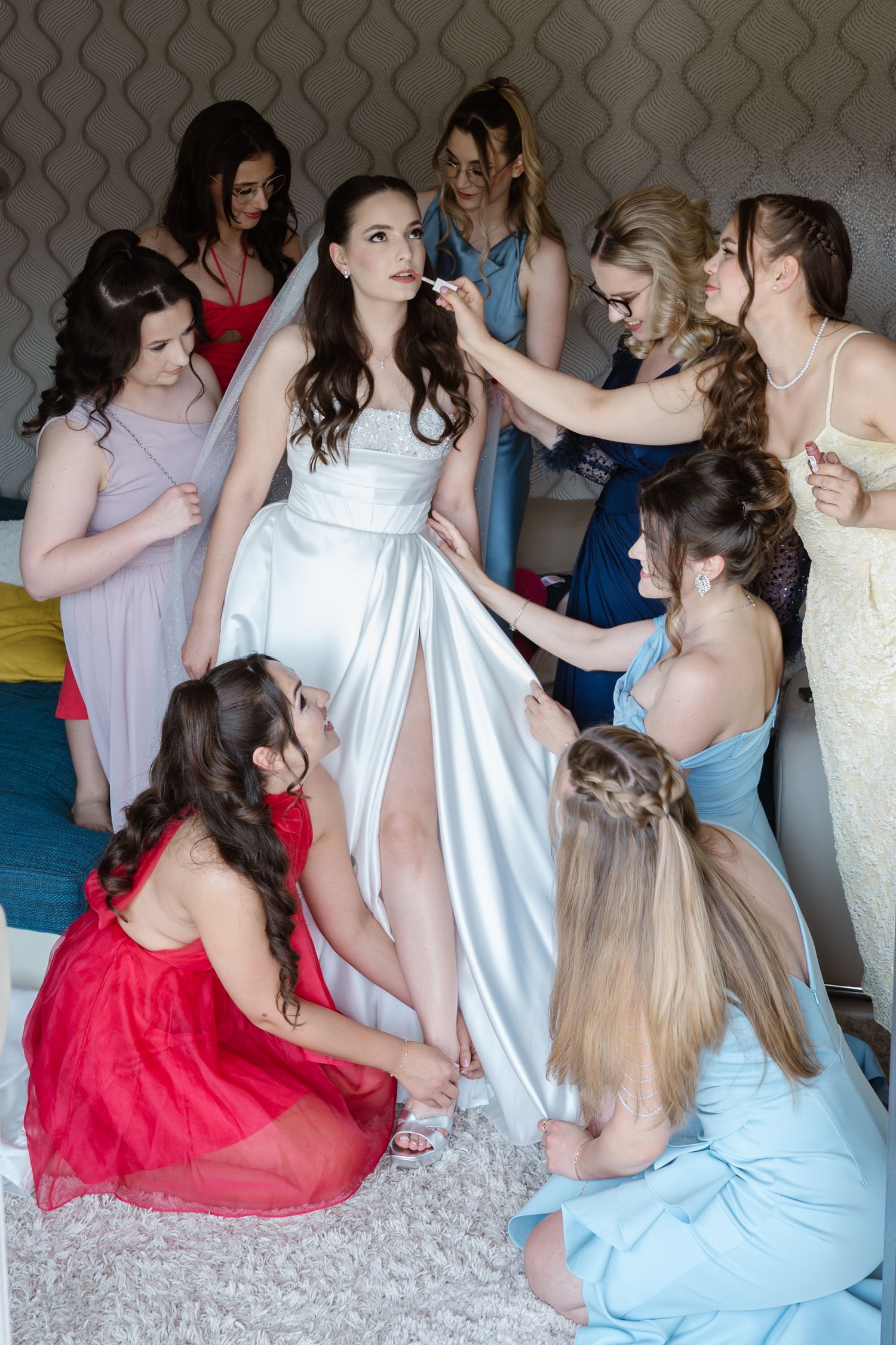 Wedding party in pastel and red dresses sitting together on a carpeted floor.