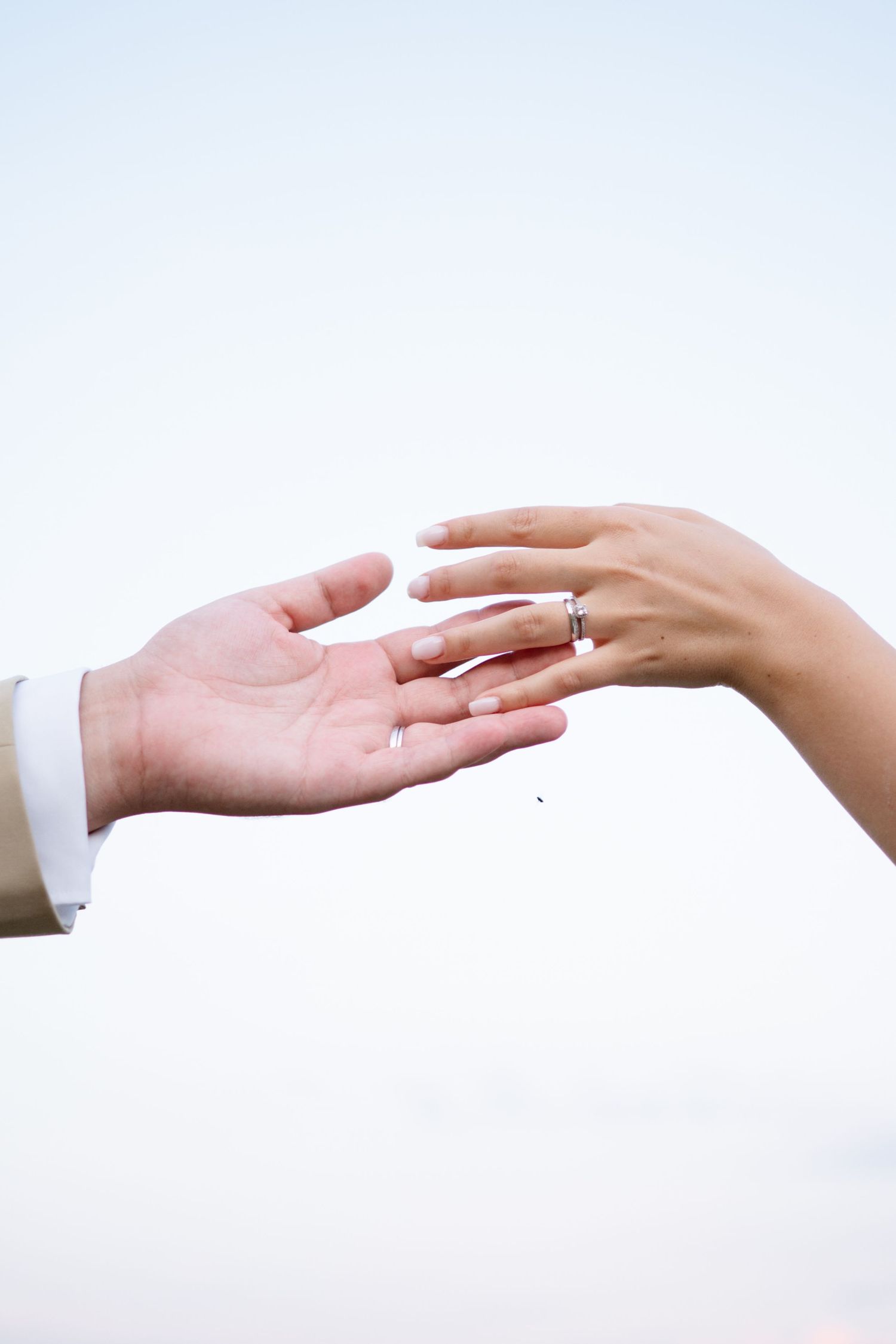Two hands reaching toward each other with a wedding ring in focus.
