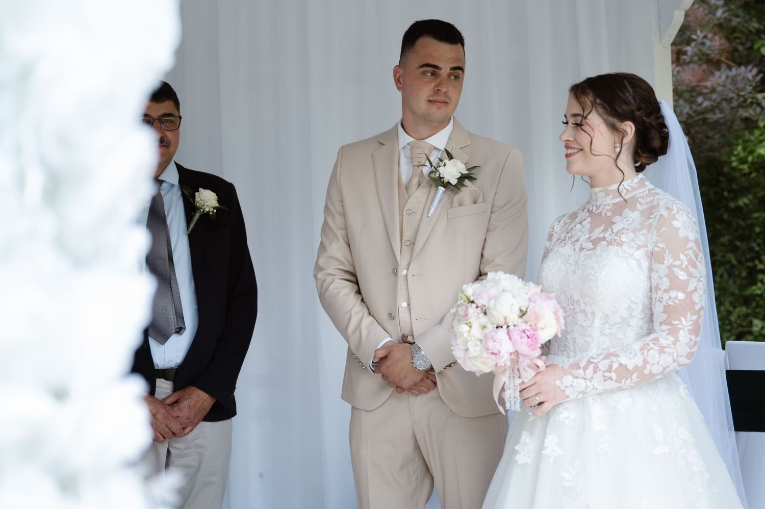 Wedding ceremony scene with white backdrop and formal attire.