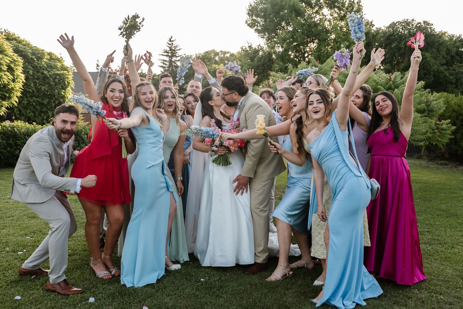Wedding party in light blue and pink dresses poses together on grass during summer celebration.