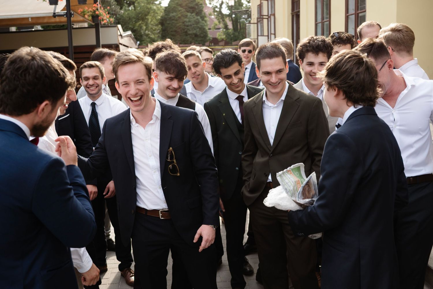 Group of young men in formal attire laughing and socializing outdoors at a school or university event.