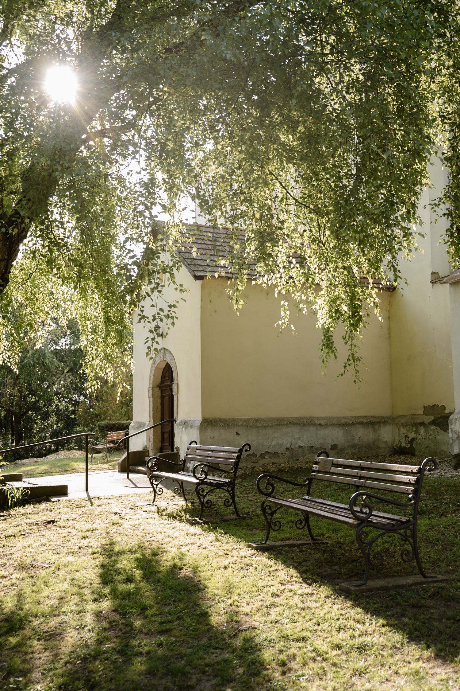 Peaceful church courtyard with benches and trees casting dappled sunlight on the ground.