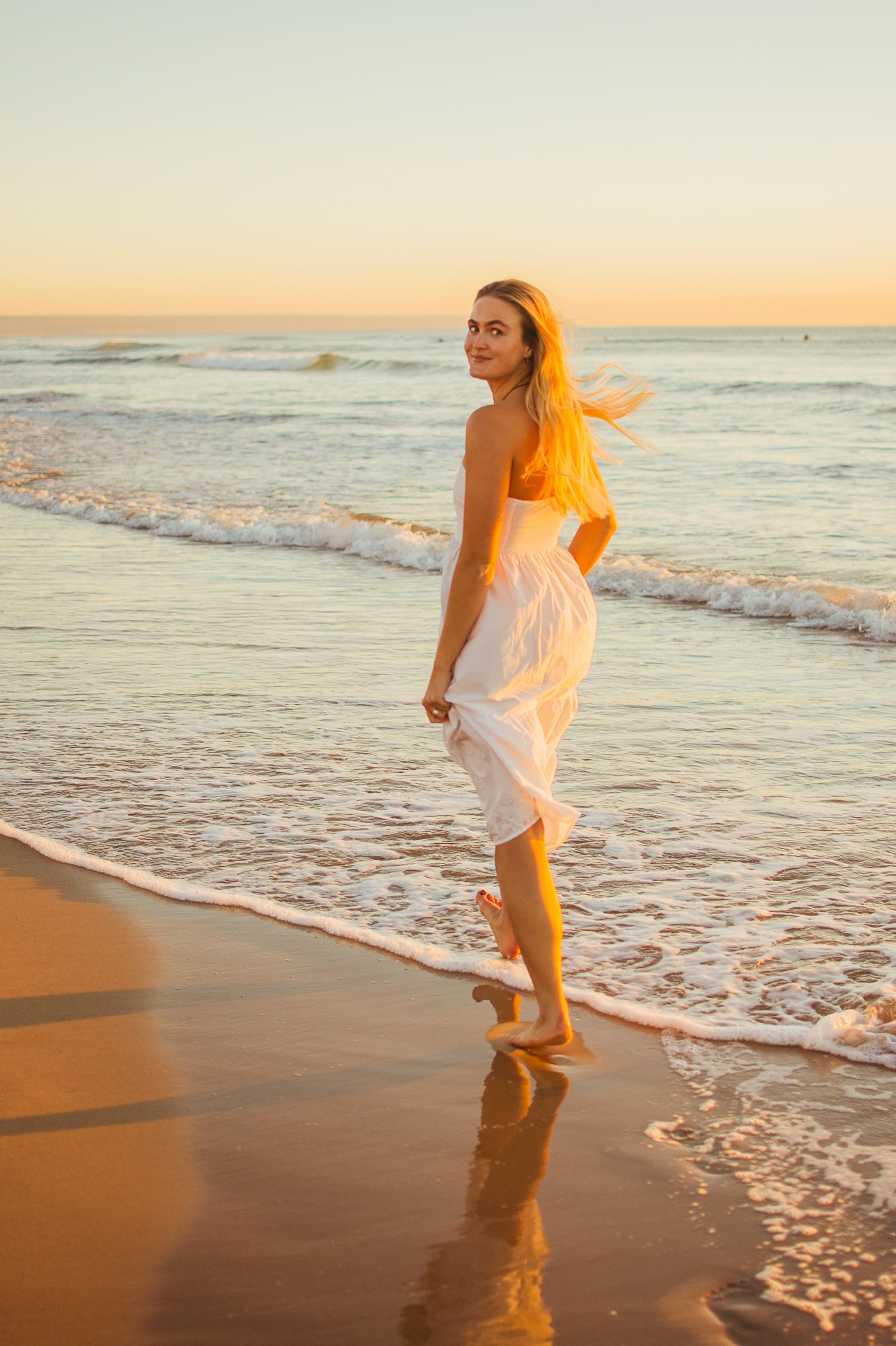 Playful moments captured of someone in a white dress dancing at the beach during sunset.