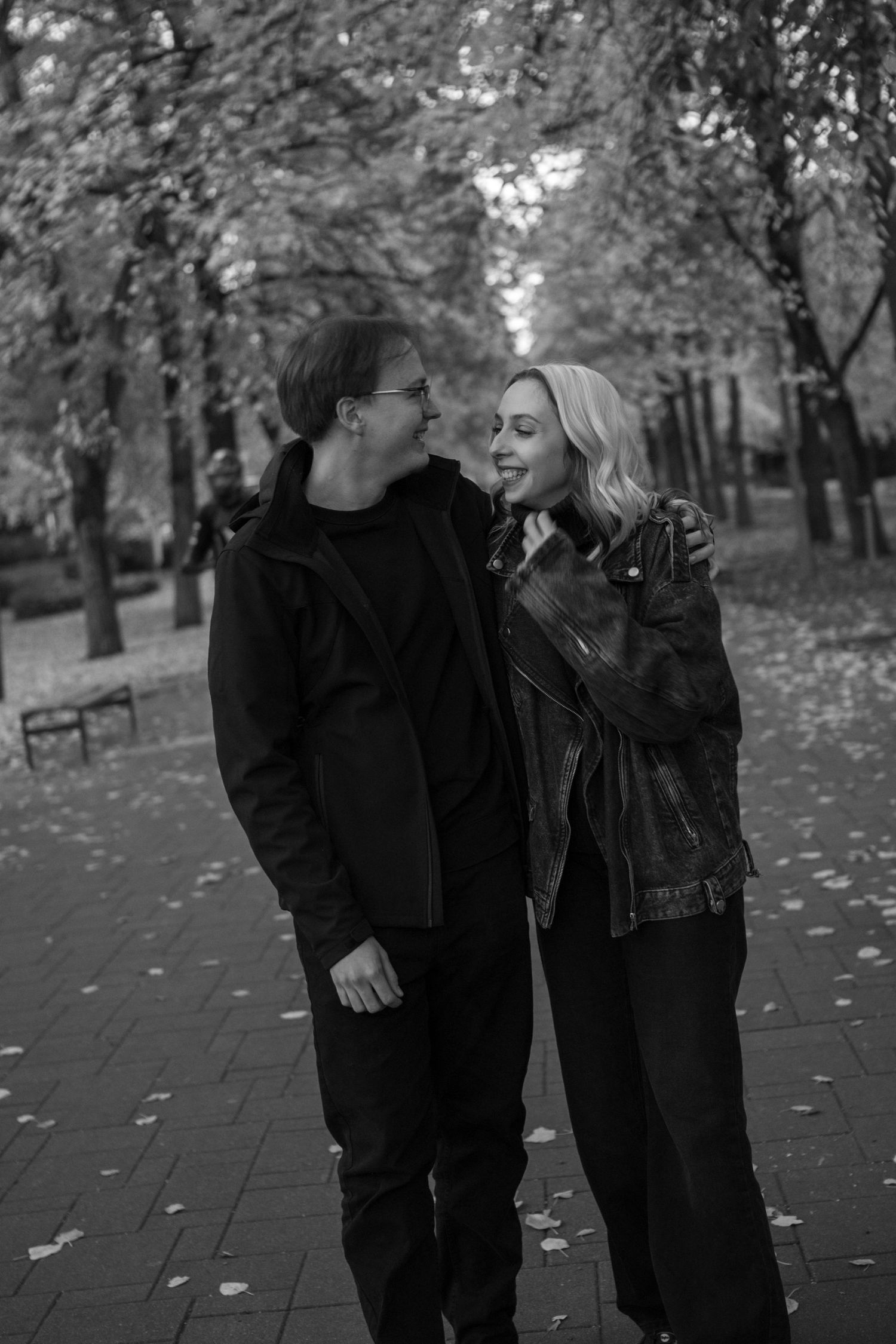 Black and white photo of couple laughing together in autumn park setting.
