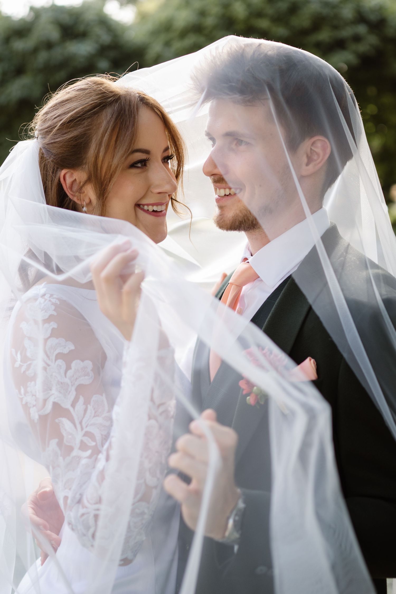 Romantic wedding portraits under a delicate white veil in a garden setting.