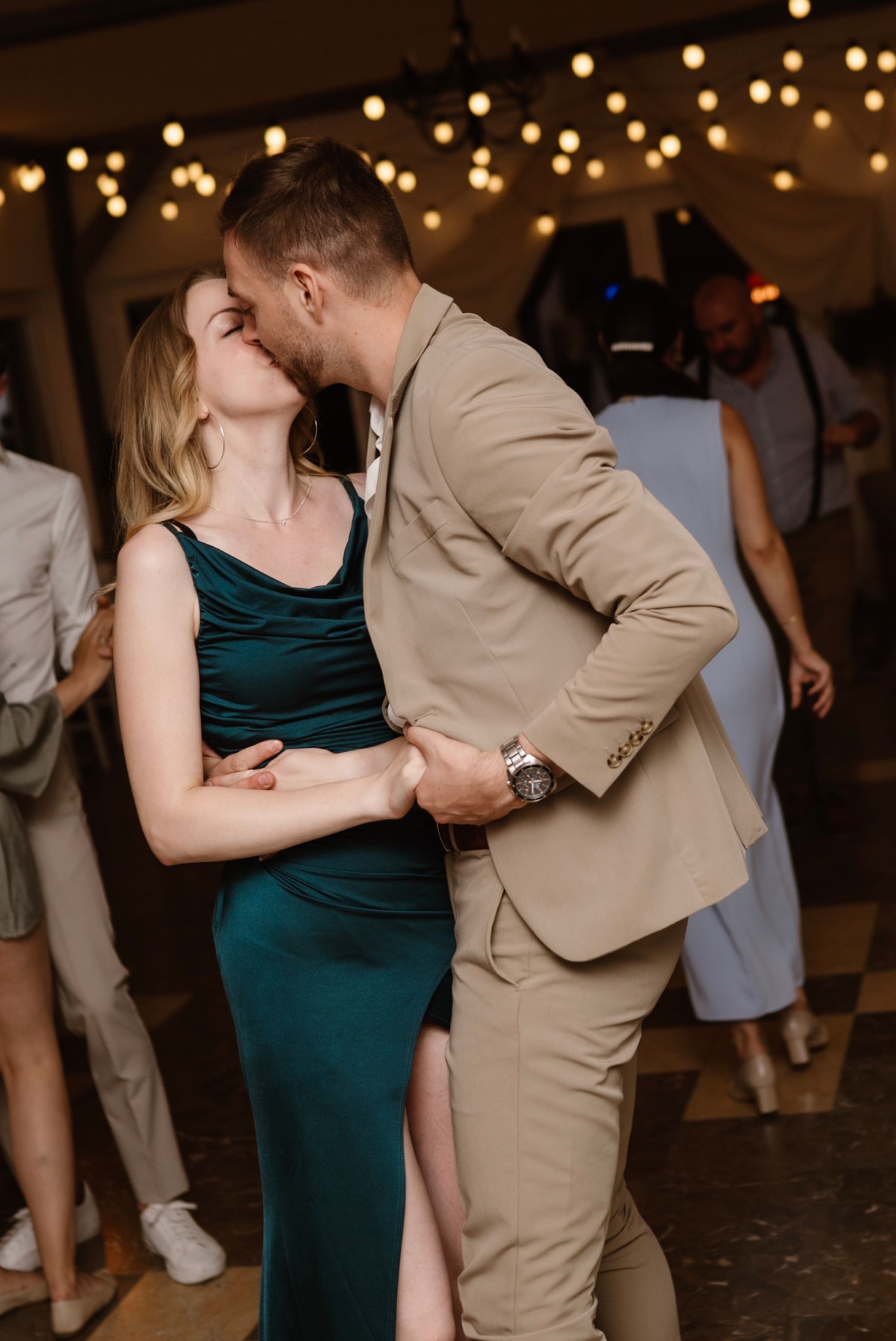 Couple sharing a romantic kiss while dancing at an elegant evening event with string lights.