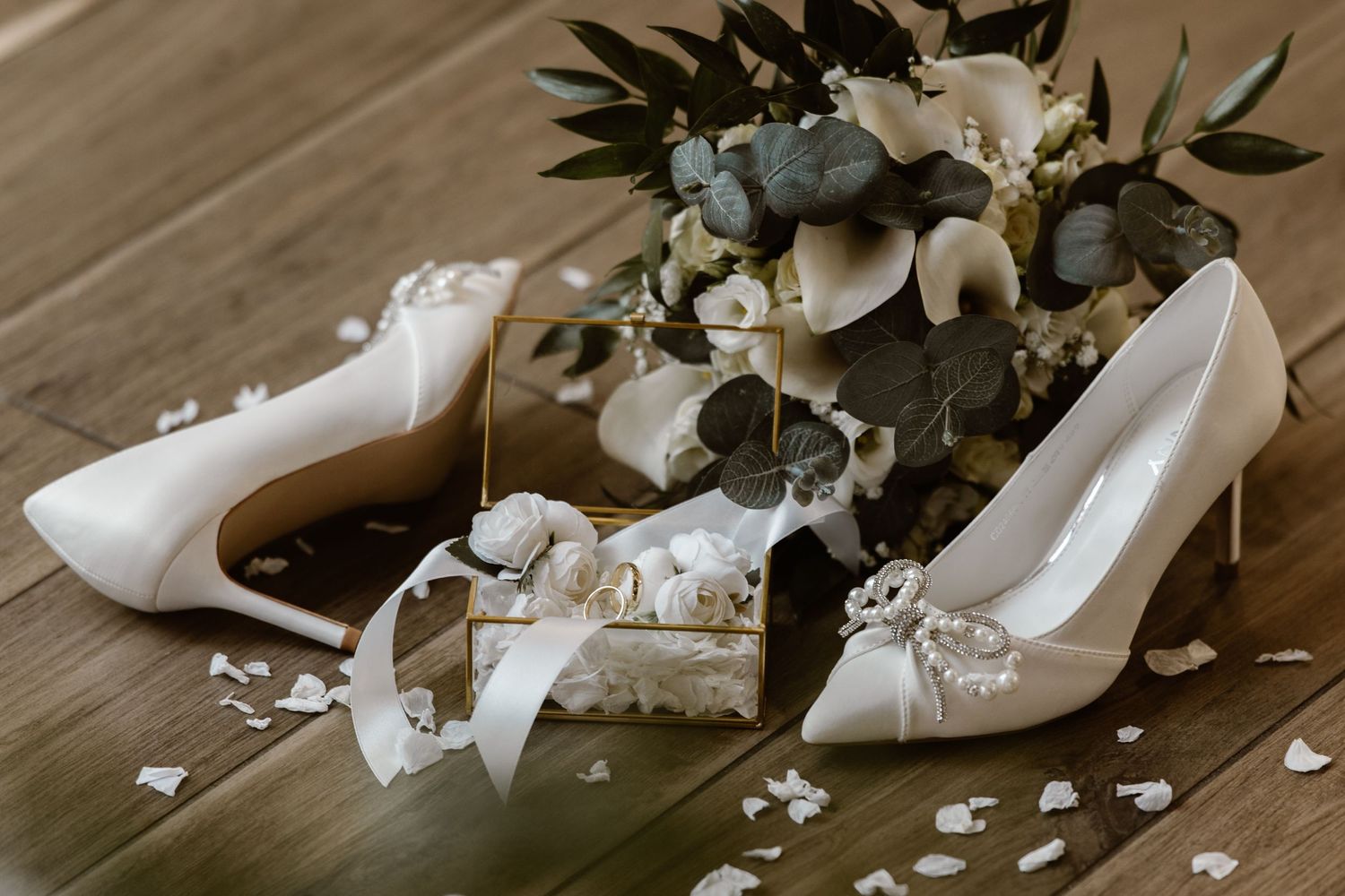 Elegant white bridal shoes displayed with floral arrangements on wooden flooring.