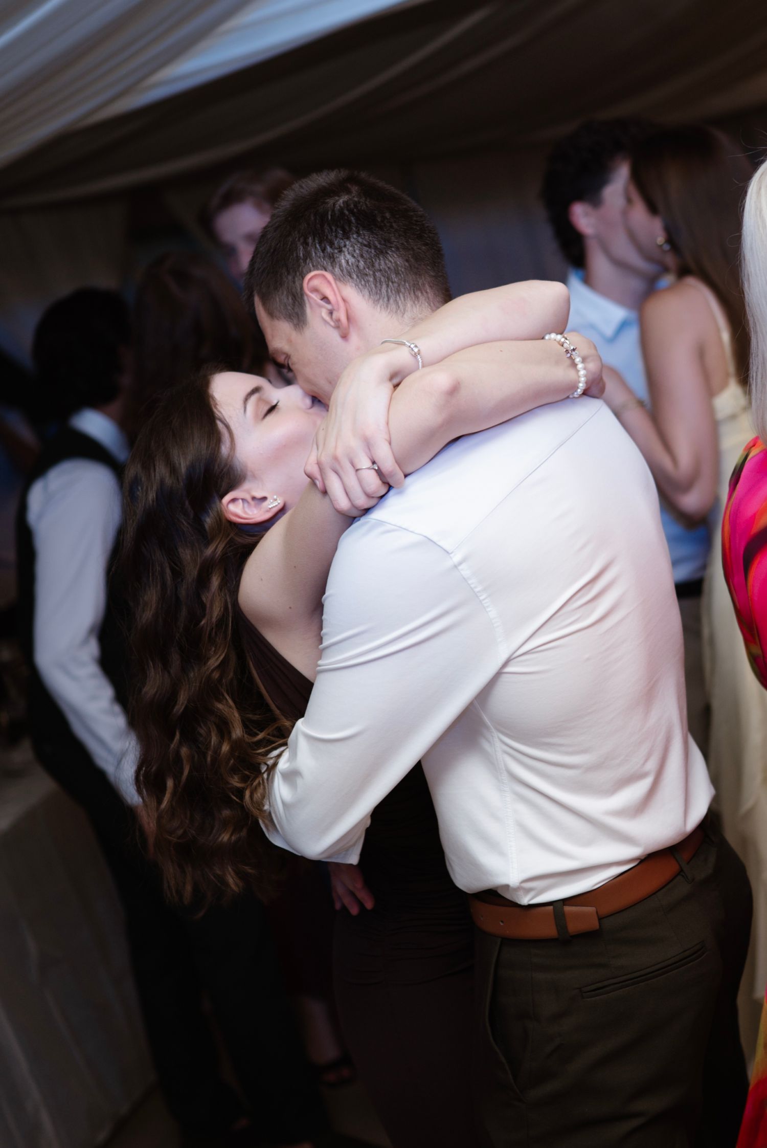 Couple sharing a romantic kiss on the dance floor at a lively wedding reception party.