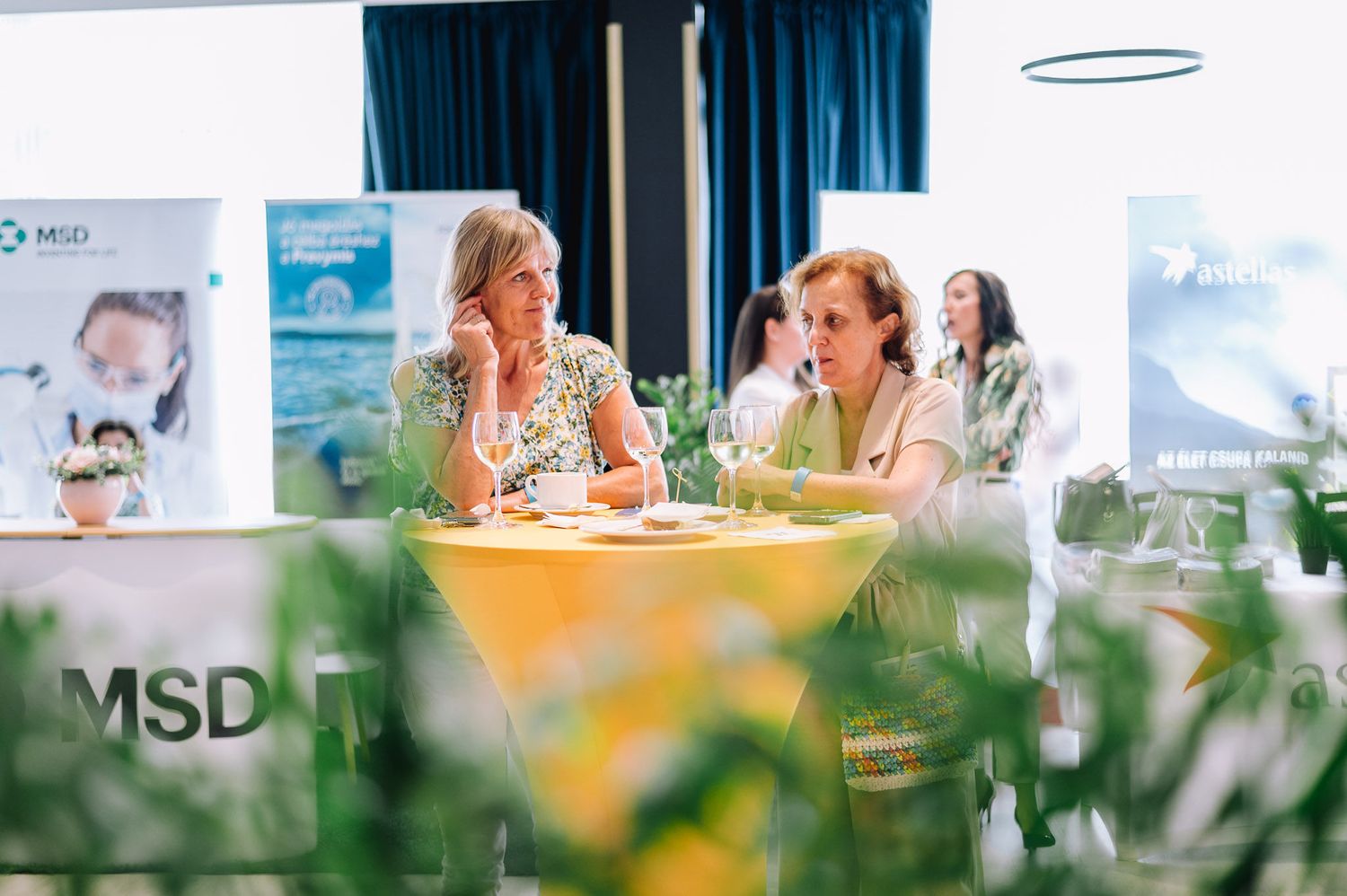 Corporate event setup with branded banners and decorative floral arrangements on tables.